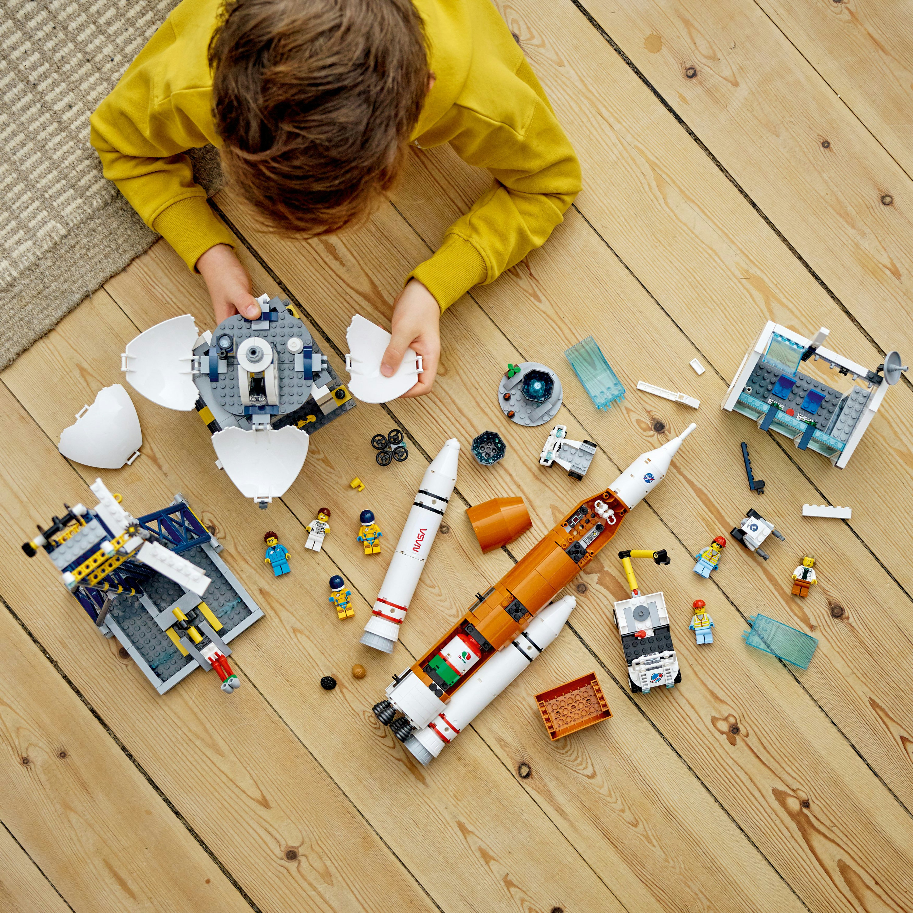 Dziecko bawiące się zestawami kosmicznymi Lego na drewnianej podłodze, w tym rakiety, pojazdy i figurki astronautów.