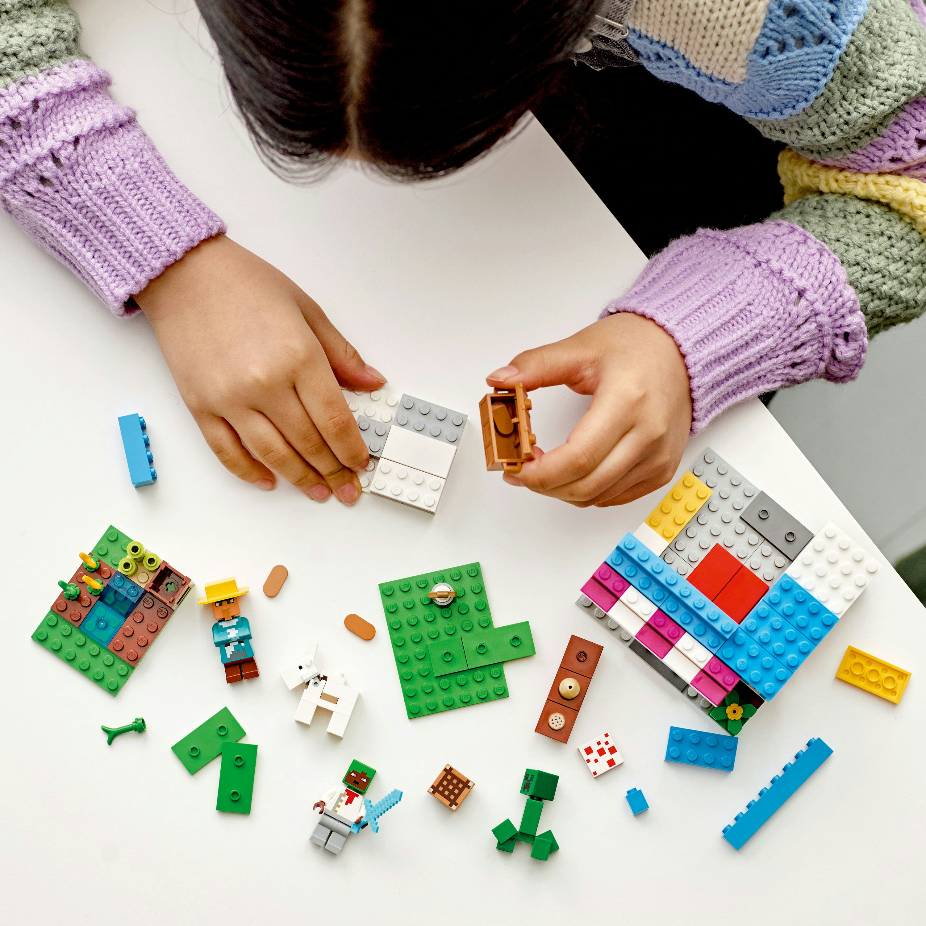 Ein Kind baut mit Lego-Steinen auf einer weißen Oberfläche, mit verschiedenen Lego-Elementen.