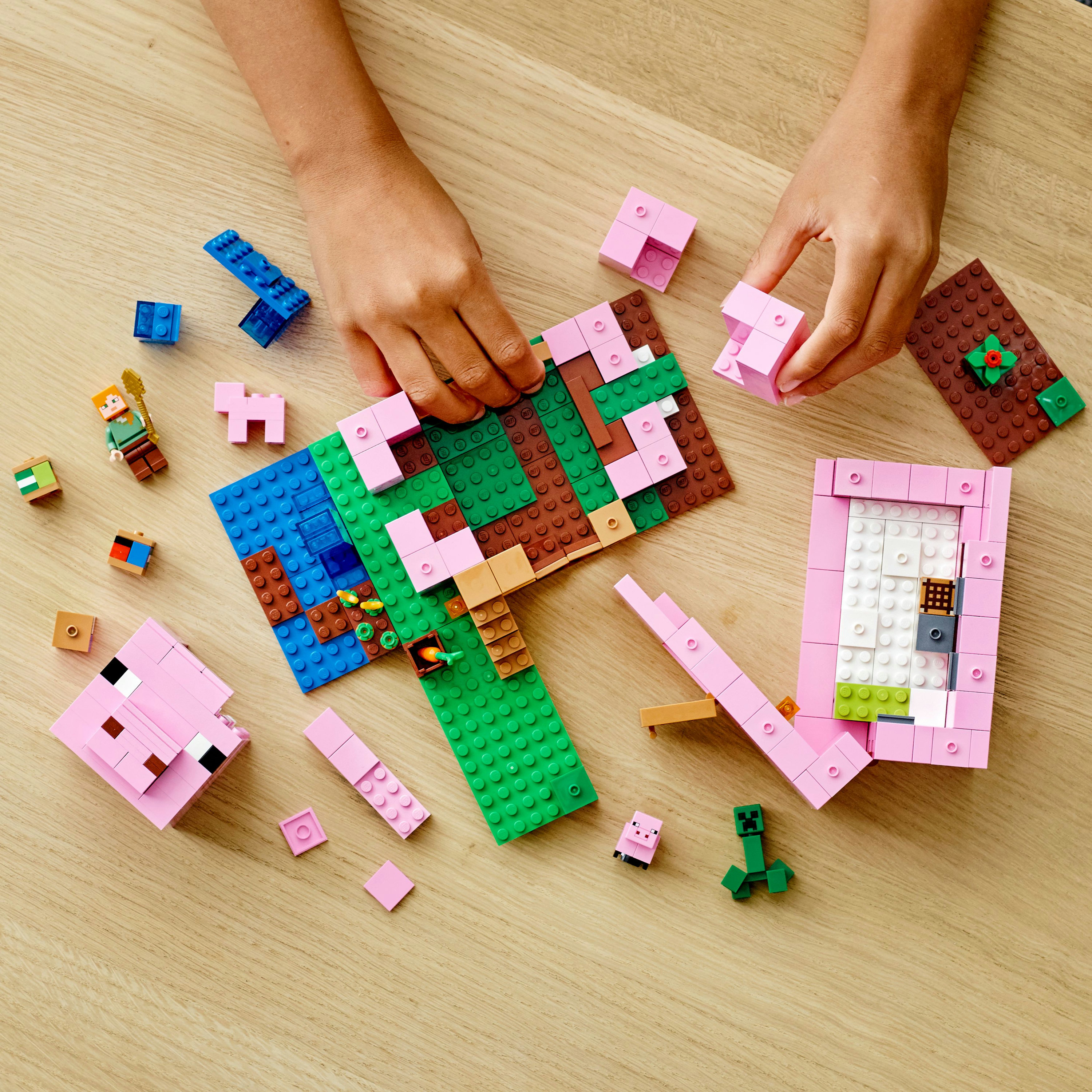 Mani che costruiscono un set LEGO Minecraft con una casa rosa. Include vari blocchi e personaggi di Minecraft.