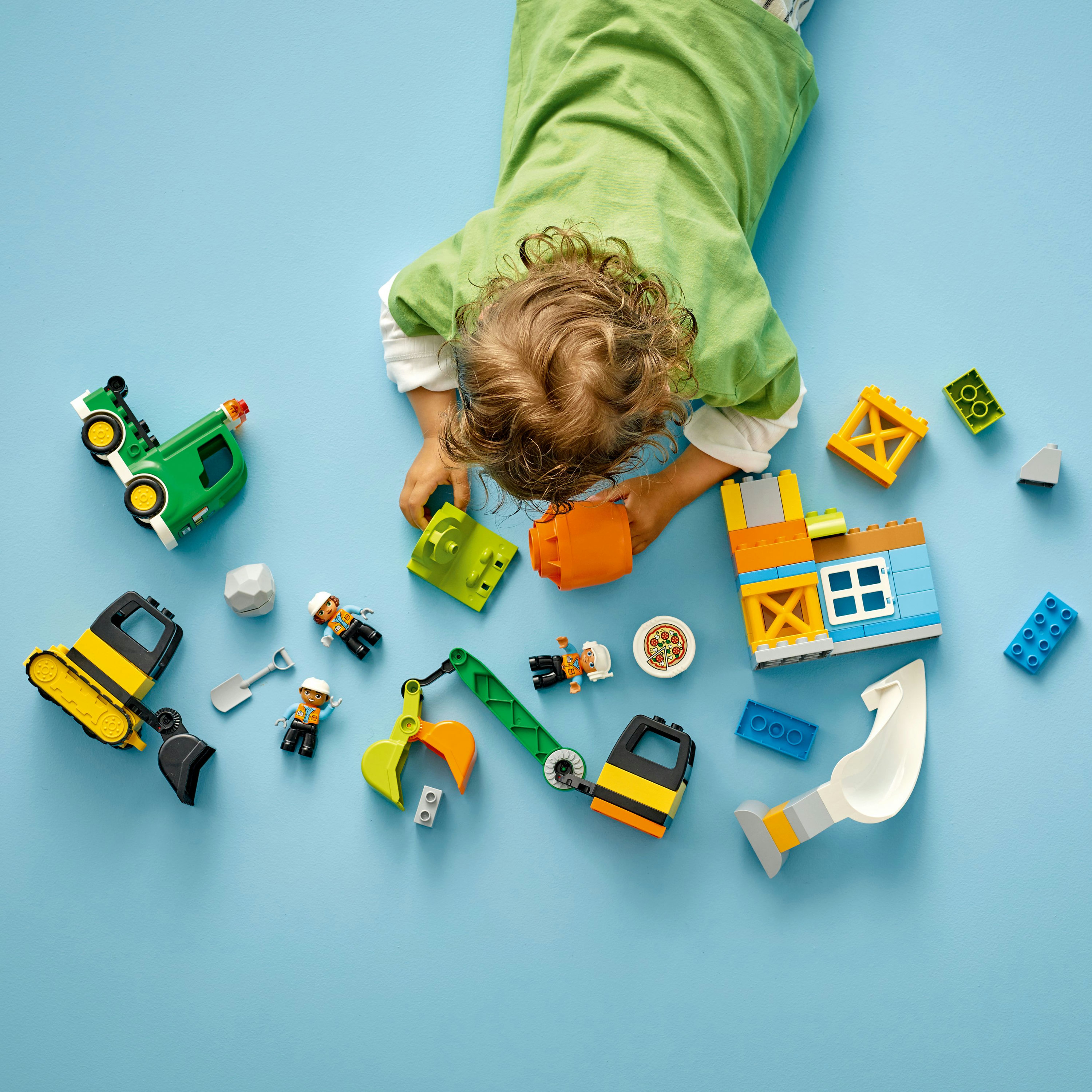 Un bambino che gioca con i mattoncini LEGO Duplo. Vari veicoli da costruzione e personaggi.