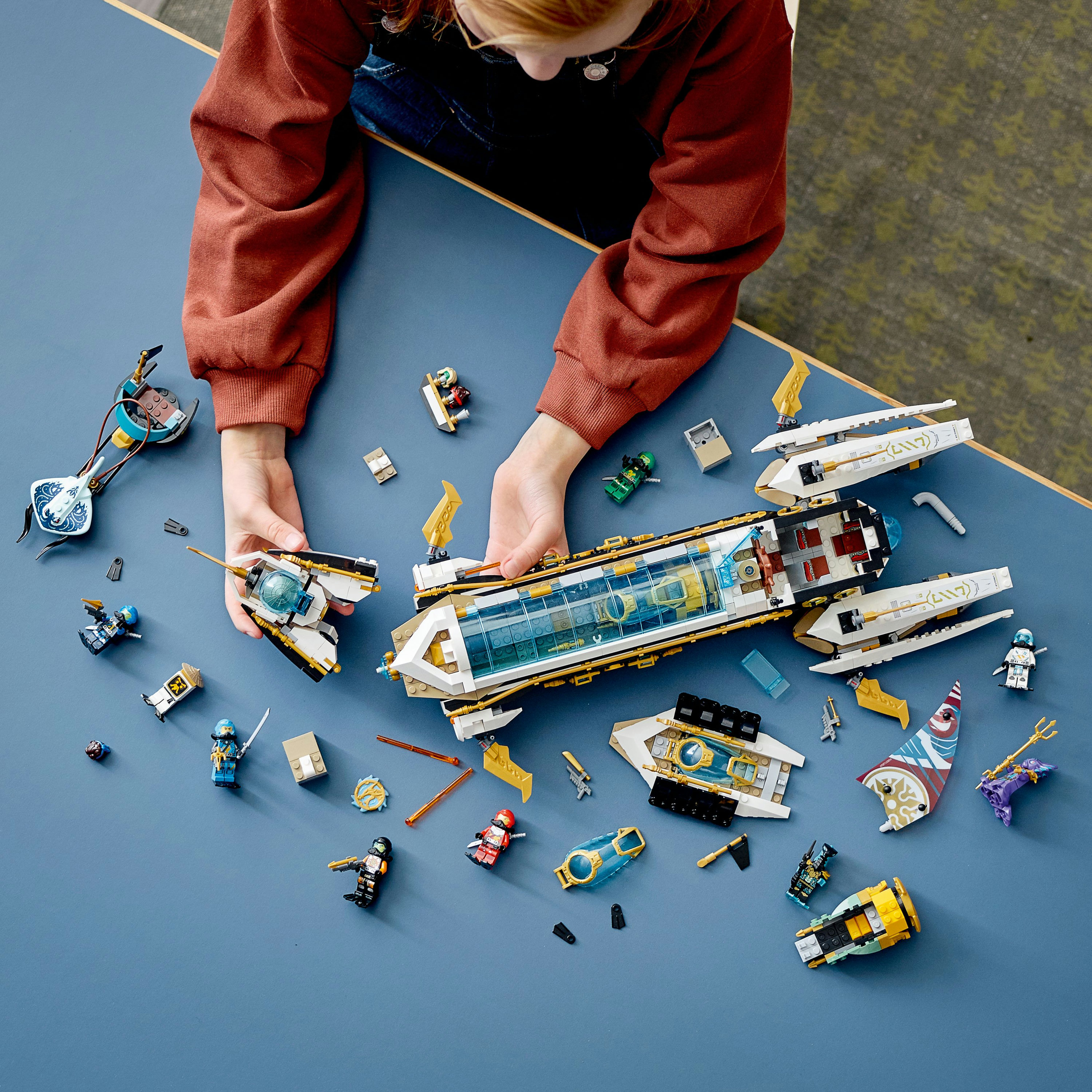 Un enfant jouant avec des ensembles Lego Ninjago. Divers véhicules et figurines Lego sur une surface bleue.