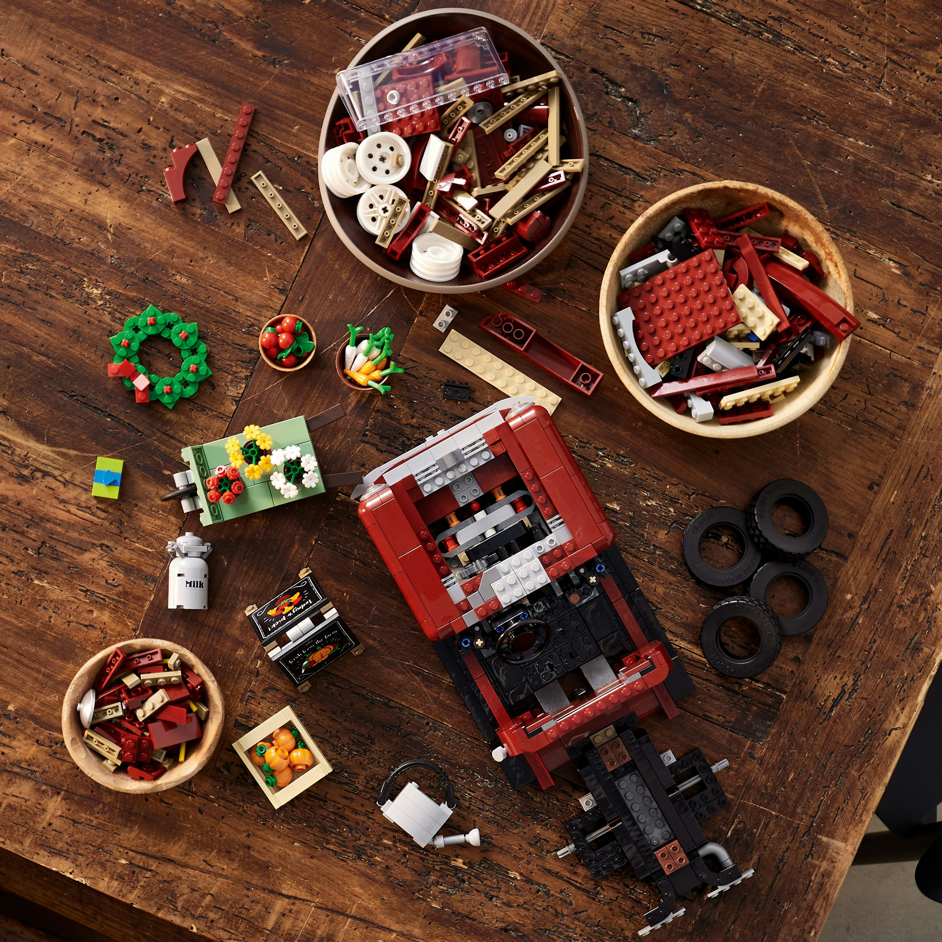 Mattoncini Lego in ciotole e un'auto rossa in costruzione su un tavolo di legno.