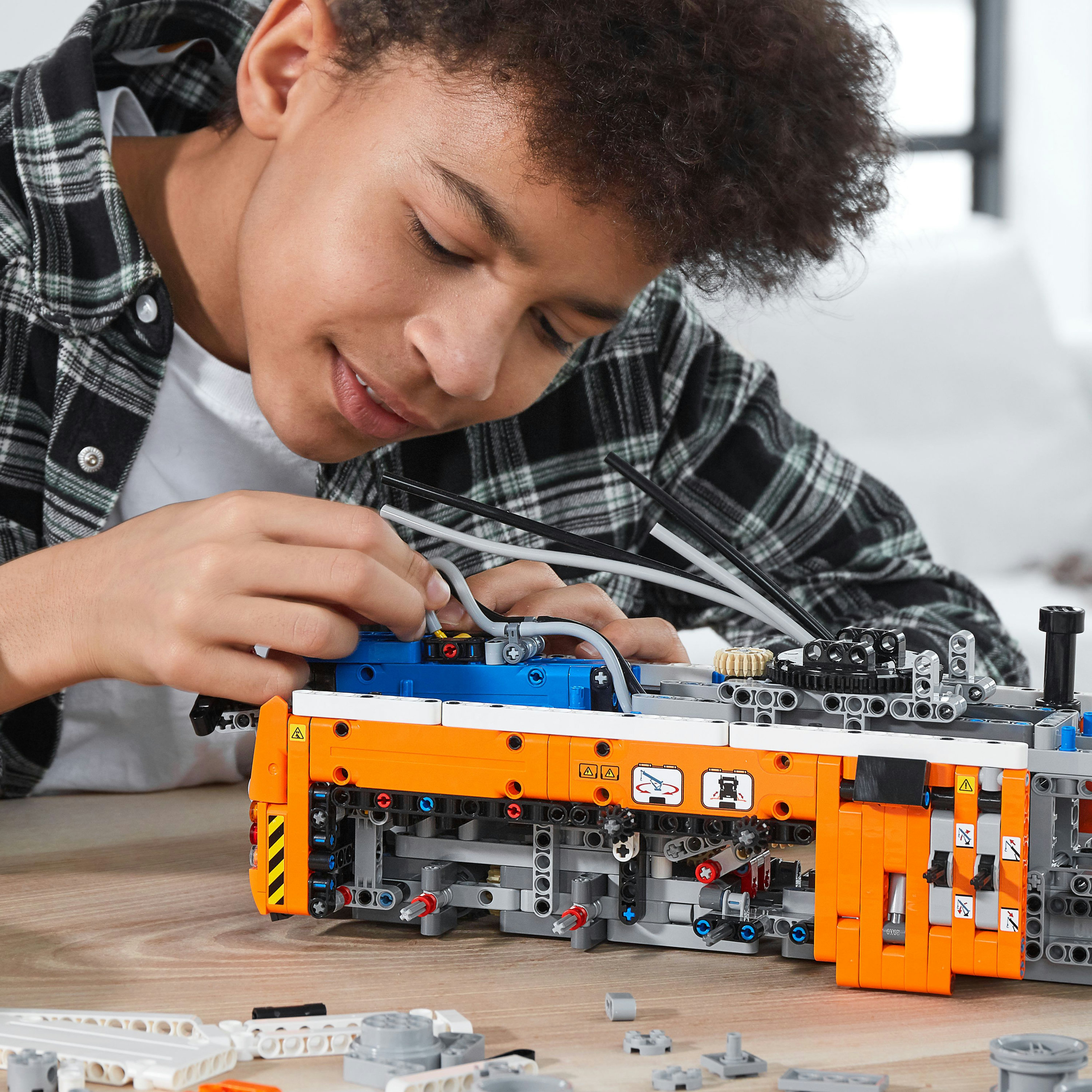 Chłopiec buduje duży pomarańczowo-niebieski model LEGO Technic. Patrzy na niego w dół.