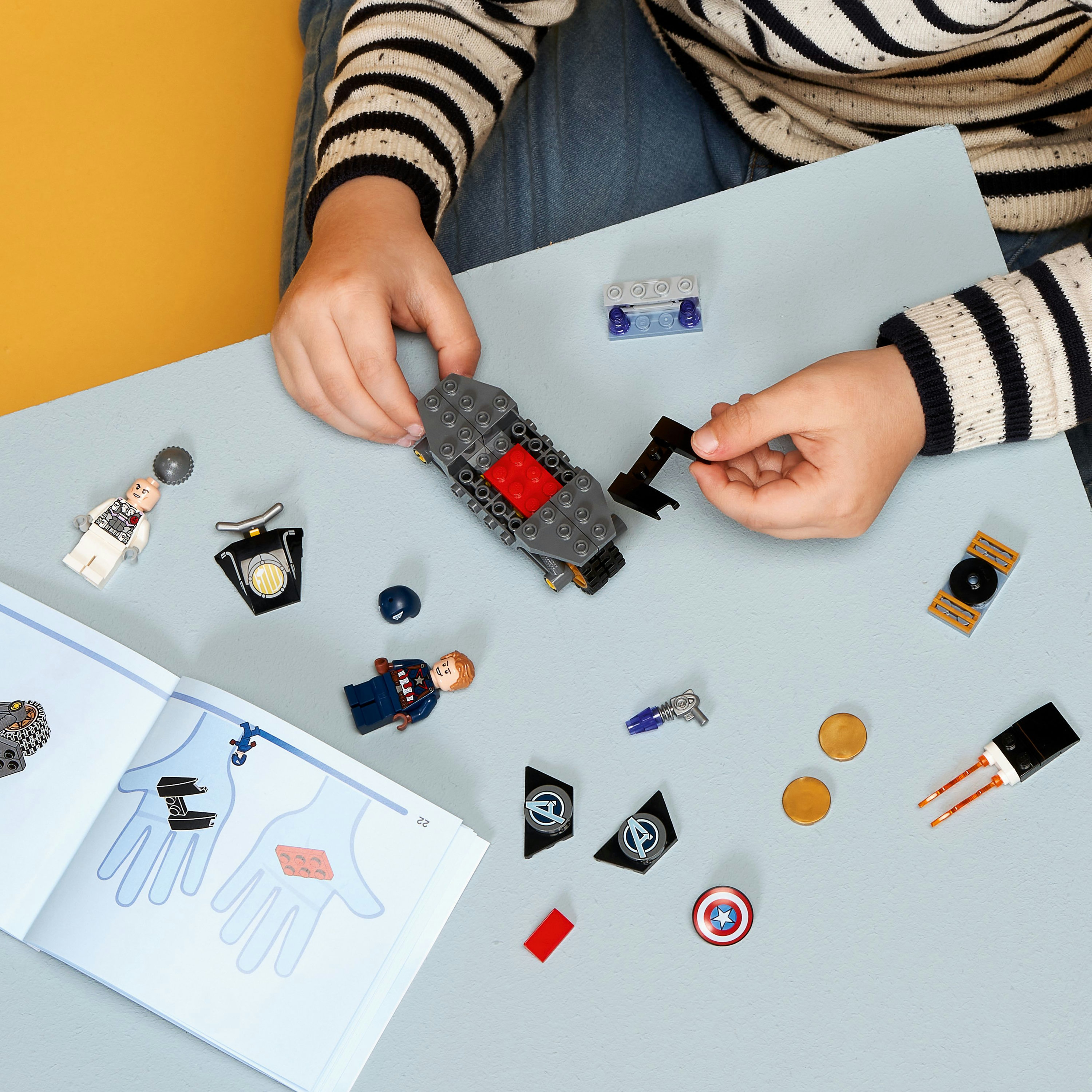 Kinderhände bauen LEGO. LEGO-Teile und Minifiguren befinden sich auf einer hellblauen Oberfläche.