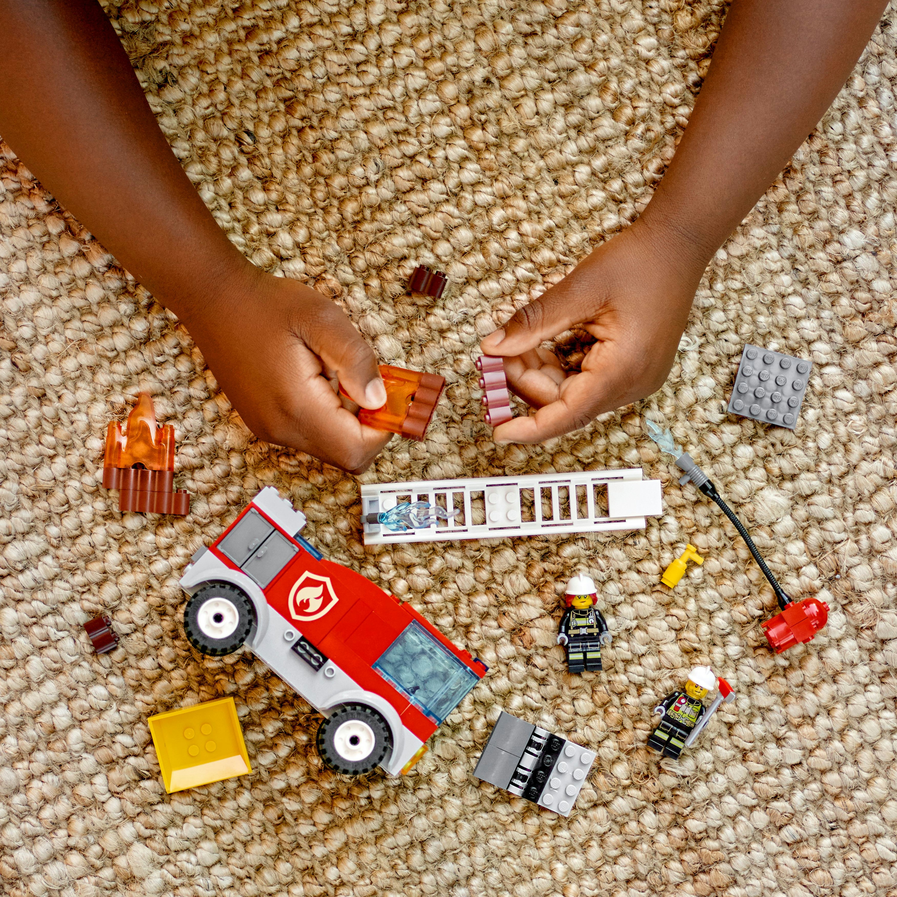 Hände eines Kindes, das Legoteile auf einem Teppich zusammensetzt.