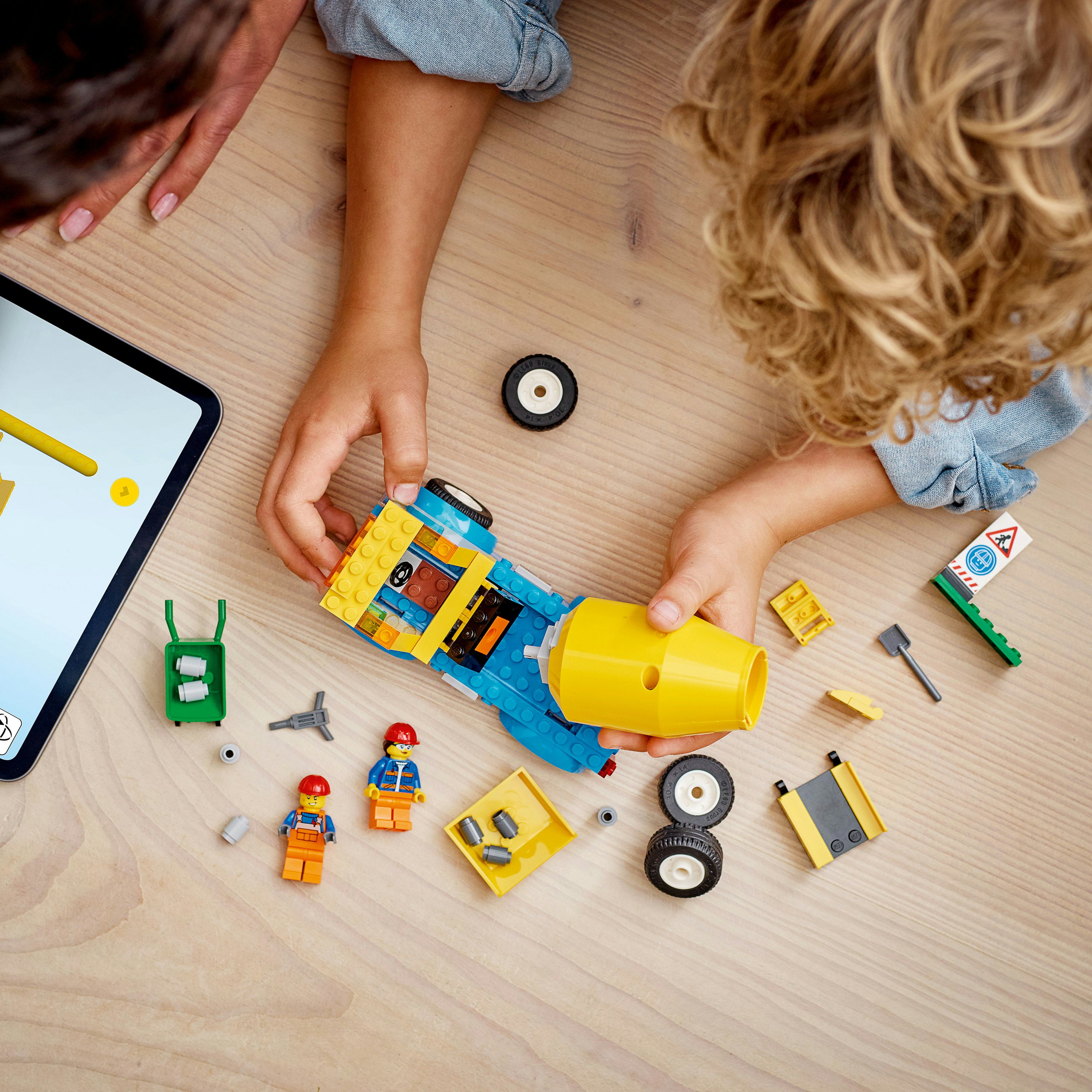 Vista superior de un niño y un adulto ensamblando un vehículo Lego sobre una superficie de madera.
