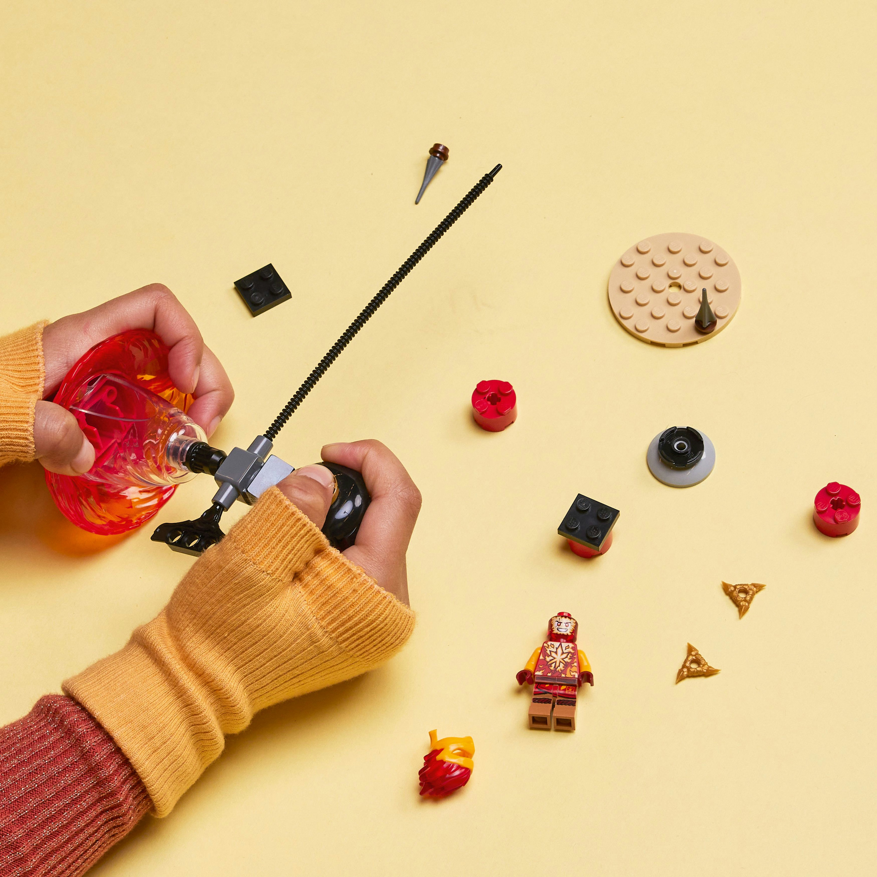 Mains jouant avec des pièces Lego, dont une toupie et des figurines, sur une surface jaune.