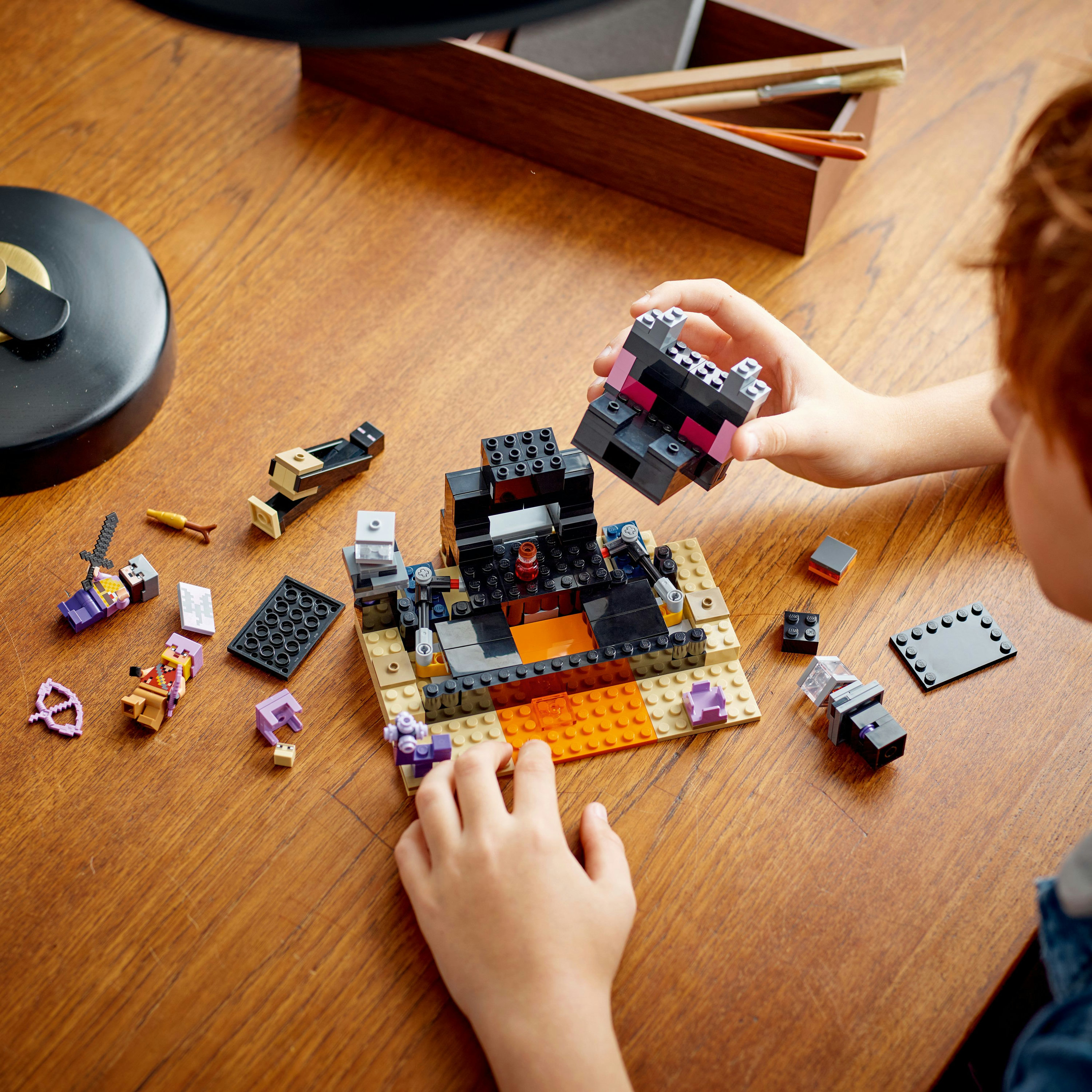 Kind spielt mit LEGO-Set. Blöcke bilden eine Struktur mit Lava und einem schwarzen Geschöpf. Viele Teile liegen herum.