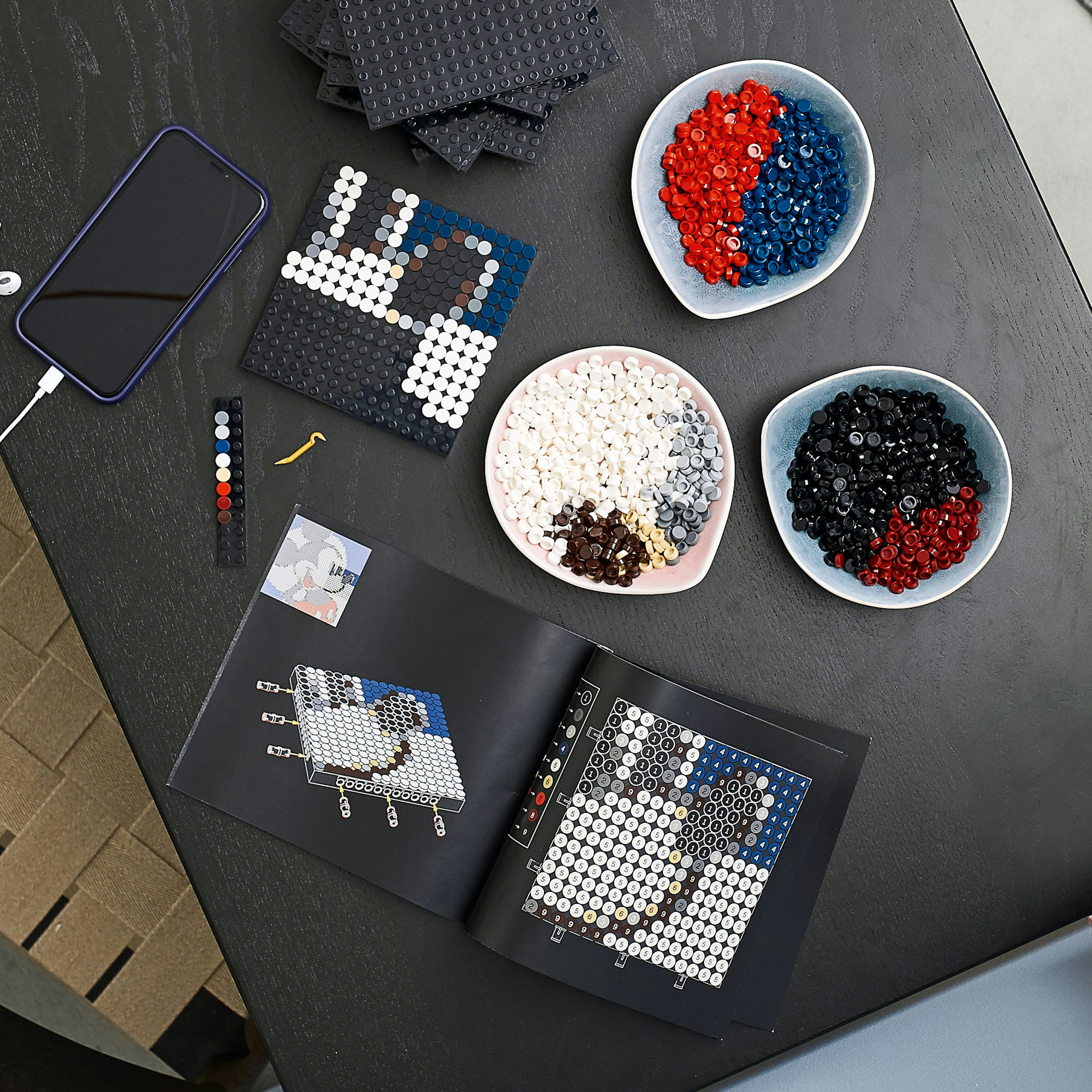Draufsicht auf einen Tisch mit Lego-Dots und Anleitungsbüchern. Telefon wird geladen.