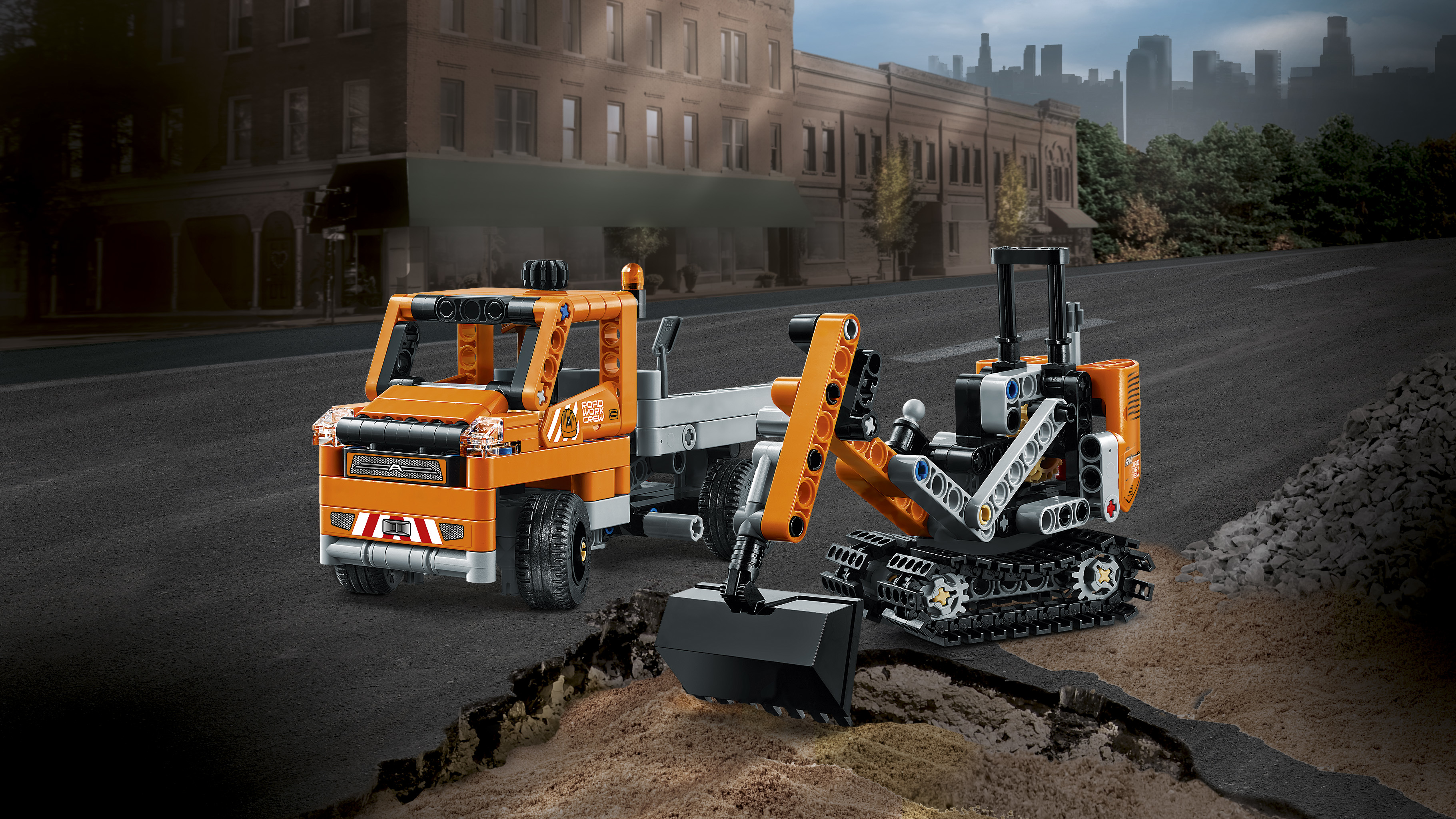 Lego vrachtwagen en graafmachine op asfalt, tegen een stedelijke achtergrond.