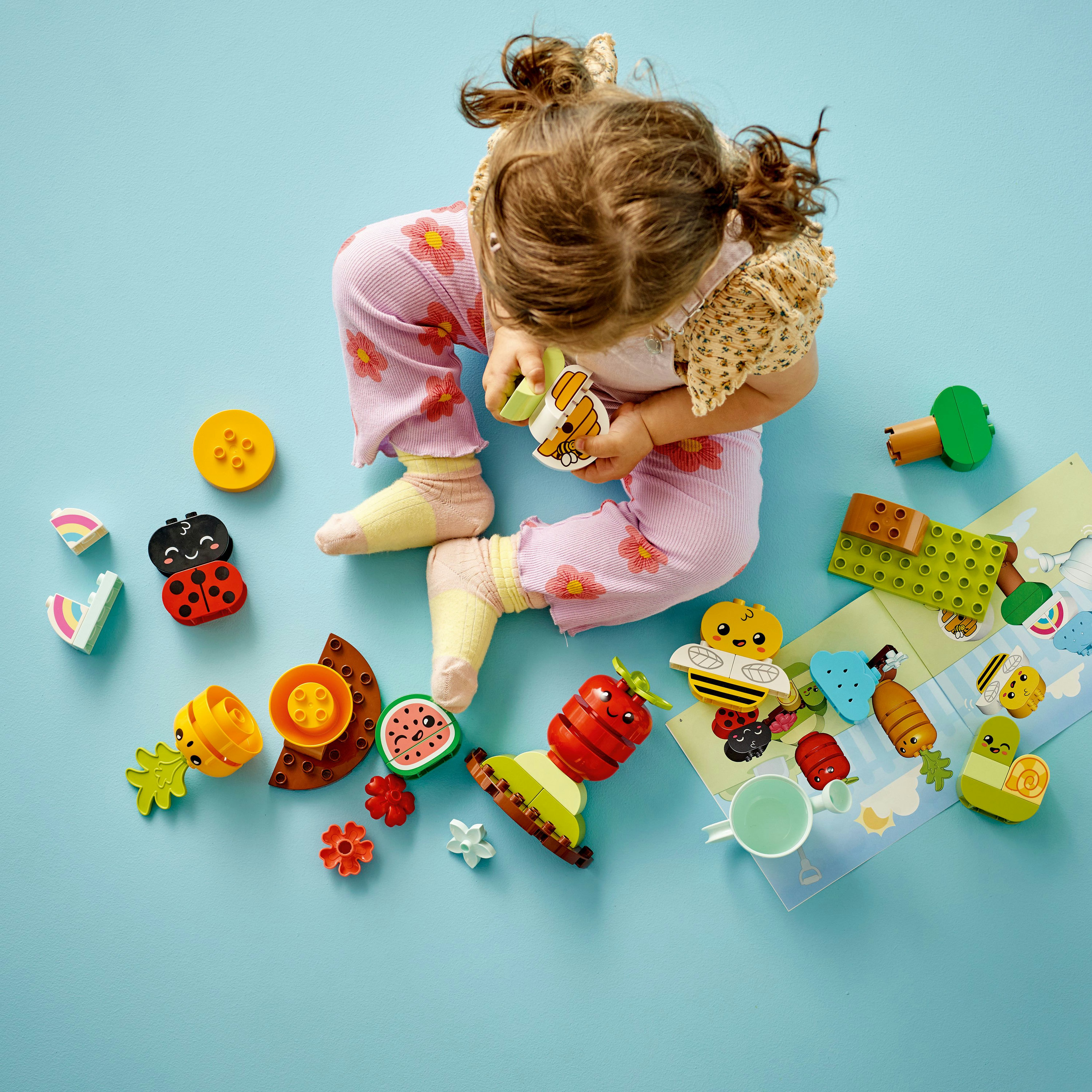 Dziecko bawiące się klockami Lego Duplo, w tym owocami, kwiatami i biedronką.