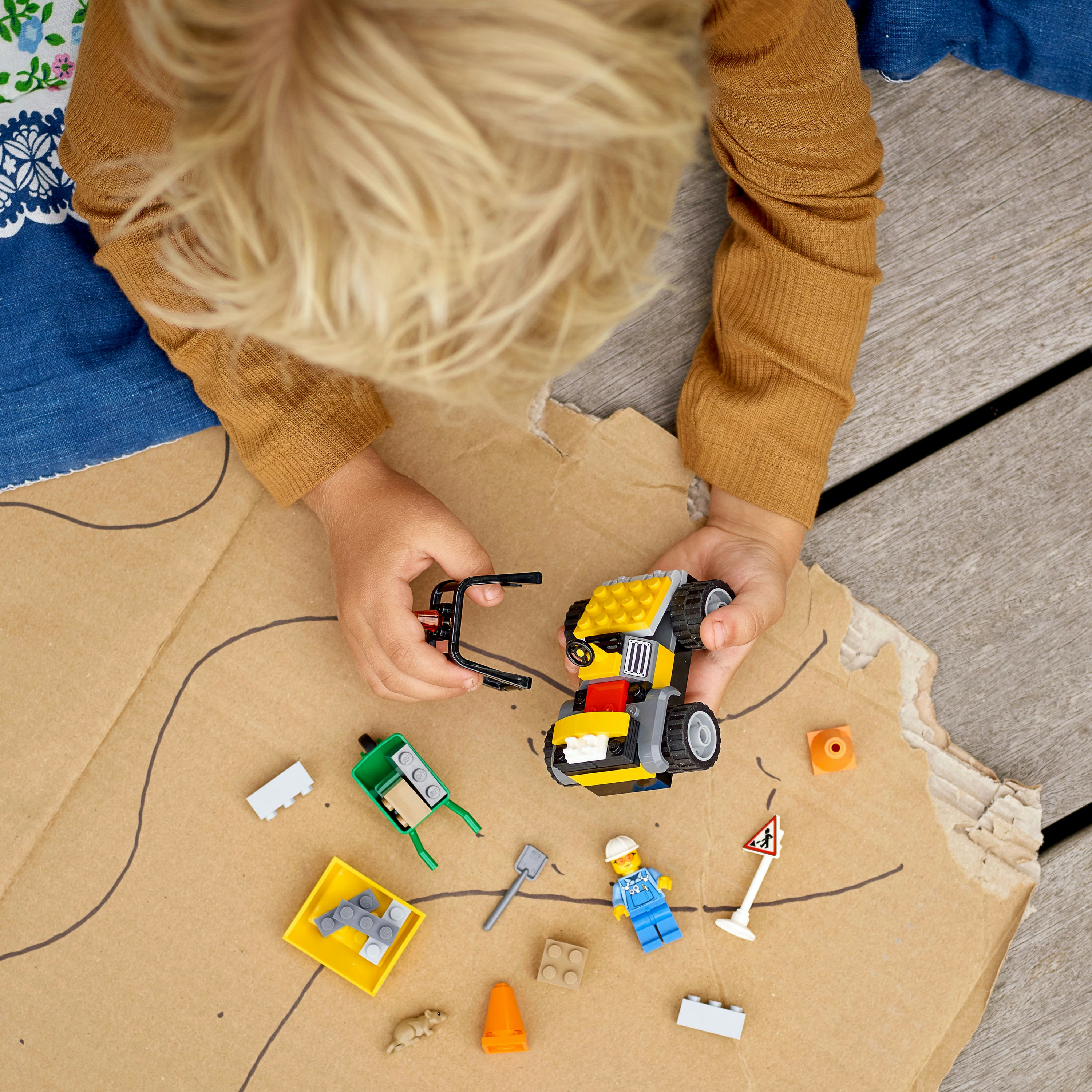 Ein Kind spielt mit einem Lego-Baufahrzeug-Set auf einer Pappkarte mit verschiedenen Lego-Elementen.