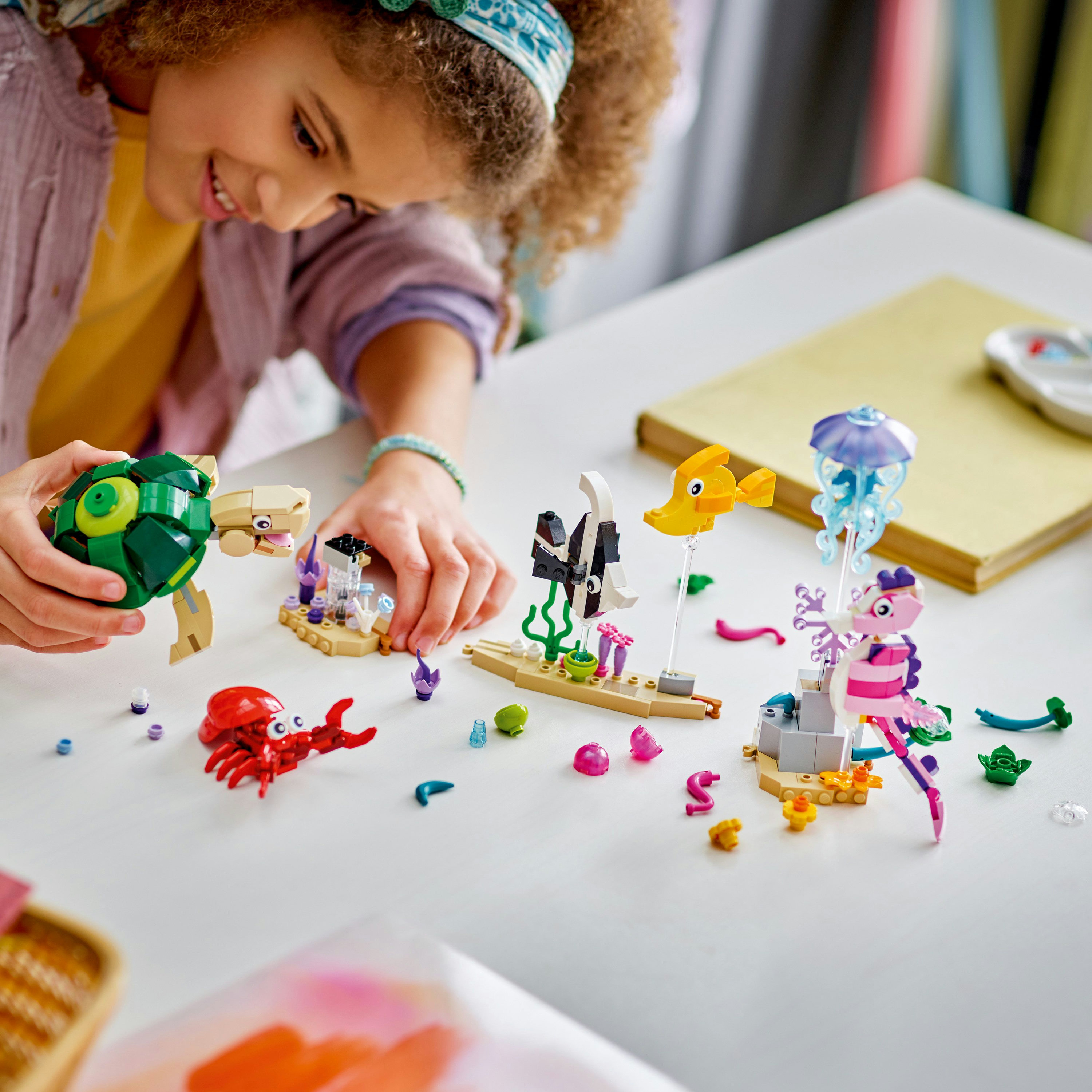 Dziecko bawiące się morskimi stworami Lego na białym stole z innymi zestawami Lego.