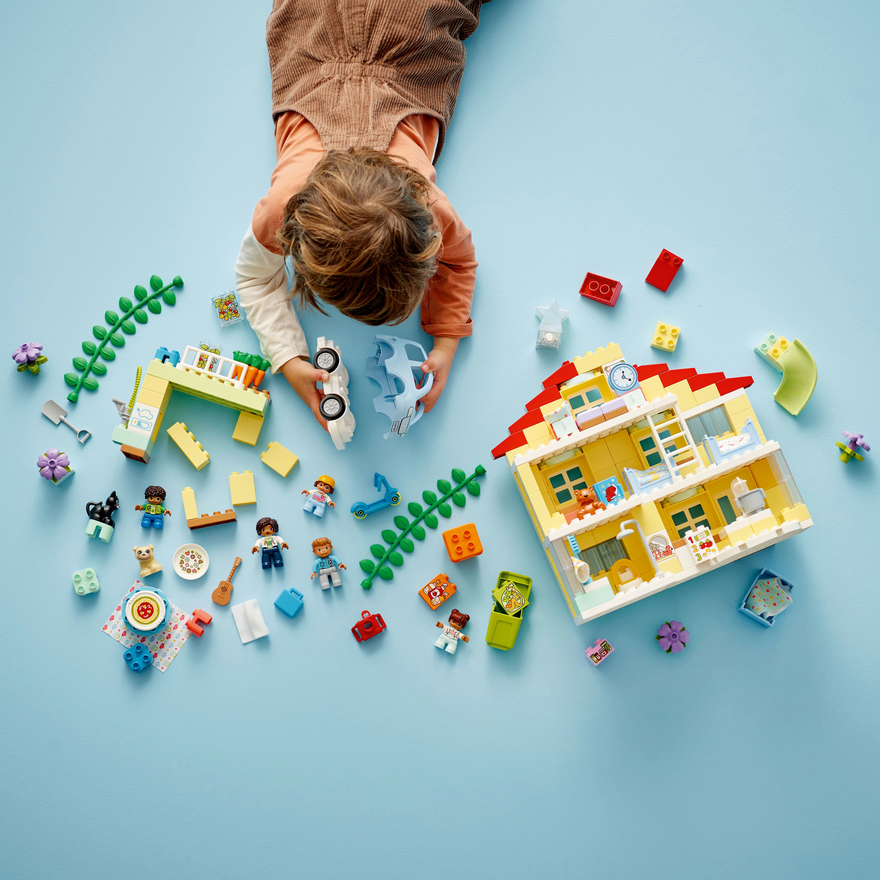 Un bambino giace su una superficie blu che gioca con blocchi Lego Duplo e una casa giocattolo.