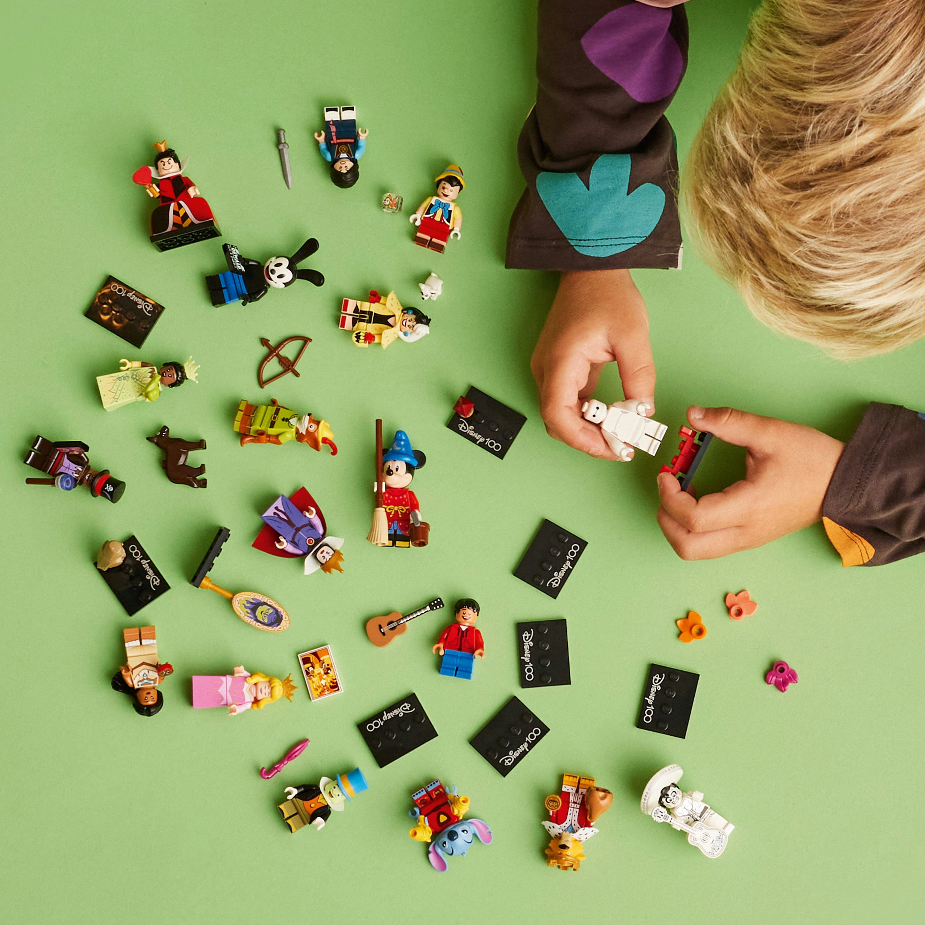 Kinderhände mit Lego-Figuren, verschiedene Charaktere auf grüner Oberfläche.