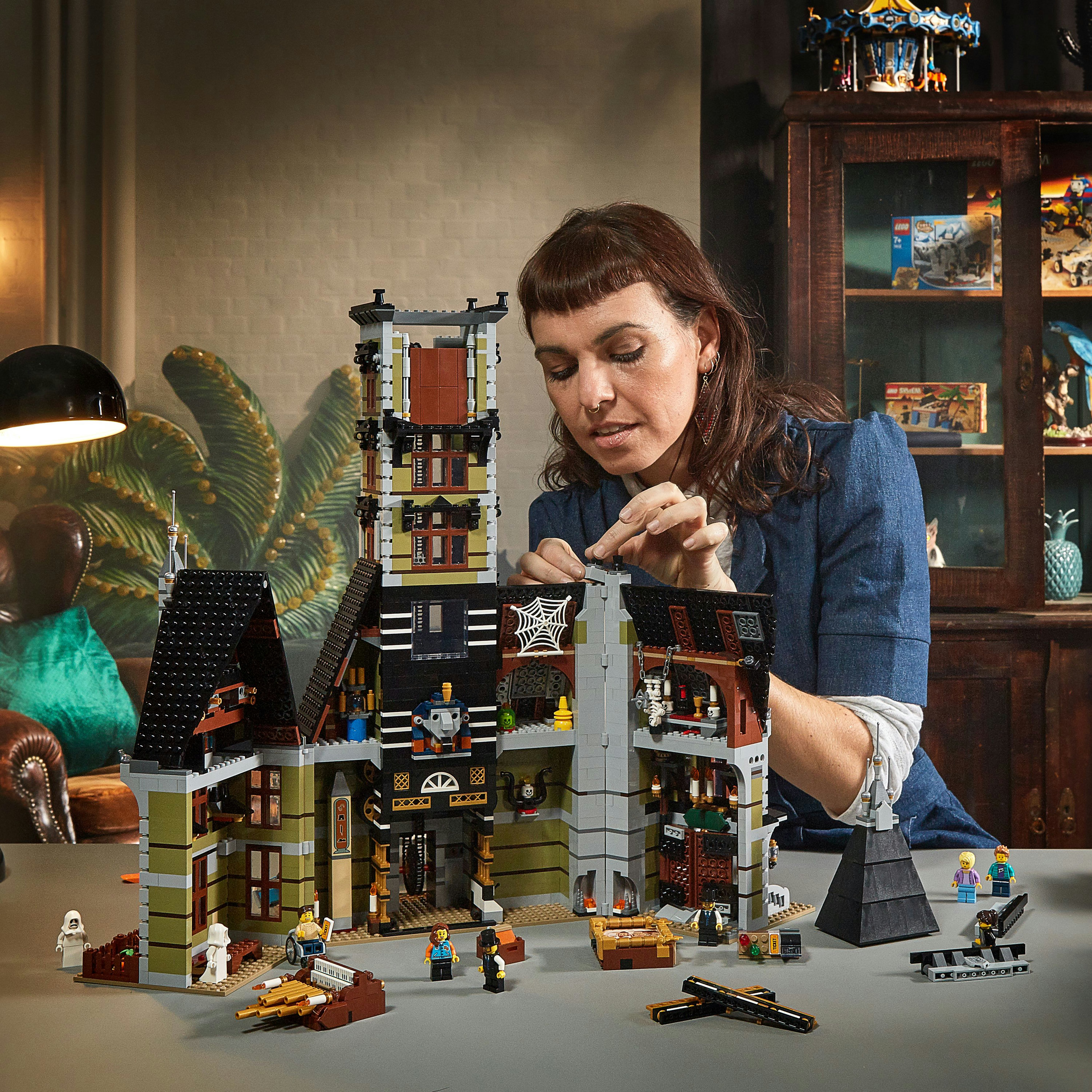 Kobieta budująca zestaw Lego z nawiedzonym domem na stole.