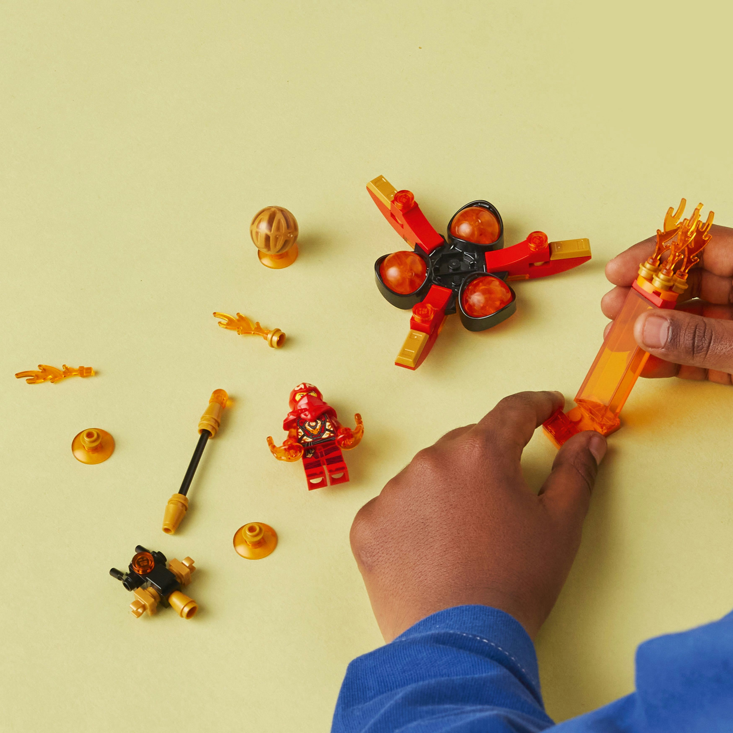 Zestaw LEGO z dłońmi dziecka składającymi zabawkę, rozrzuconymi klockami Lego i żółtą powierzchnią.