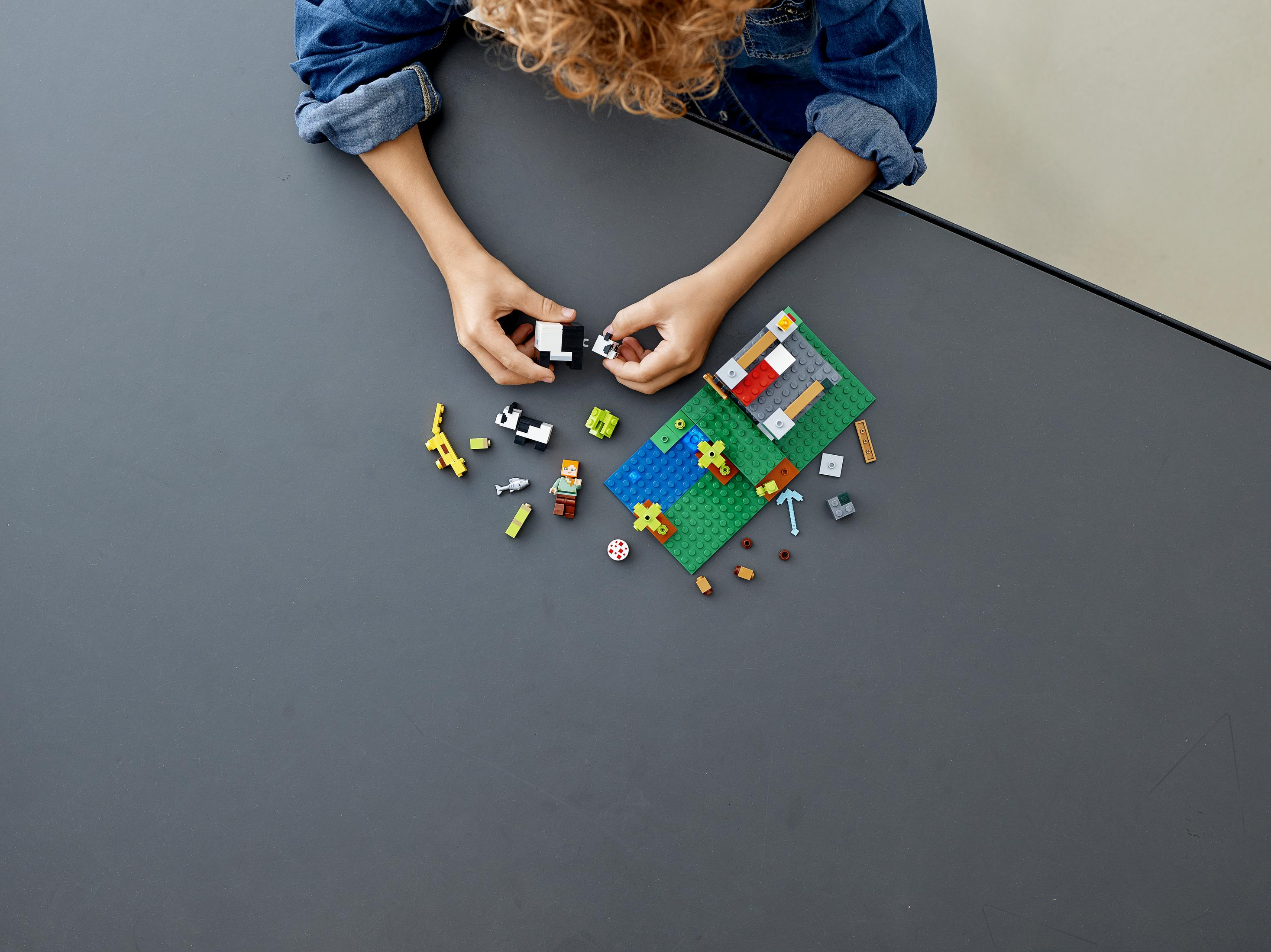 Dziecko bawi się Lego Minecraft na szarym stole. Rozrzucone różne klocki.