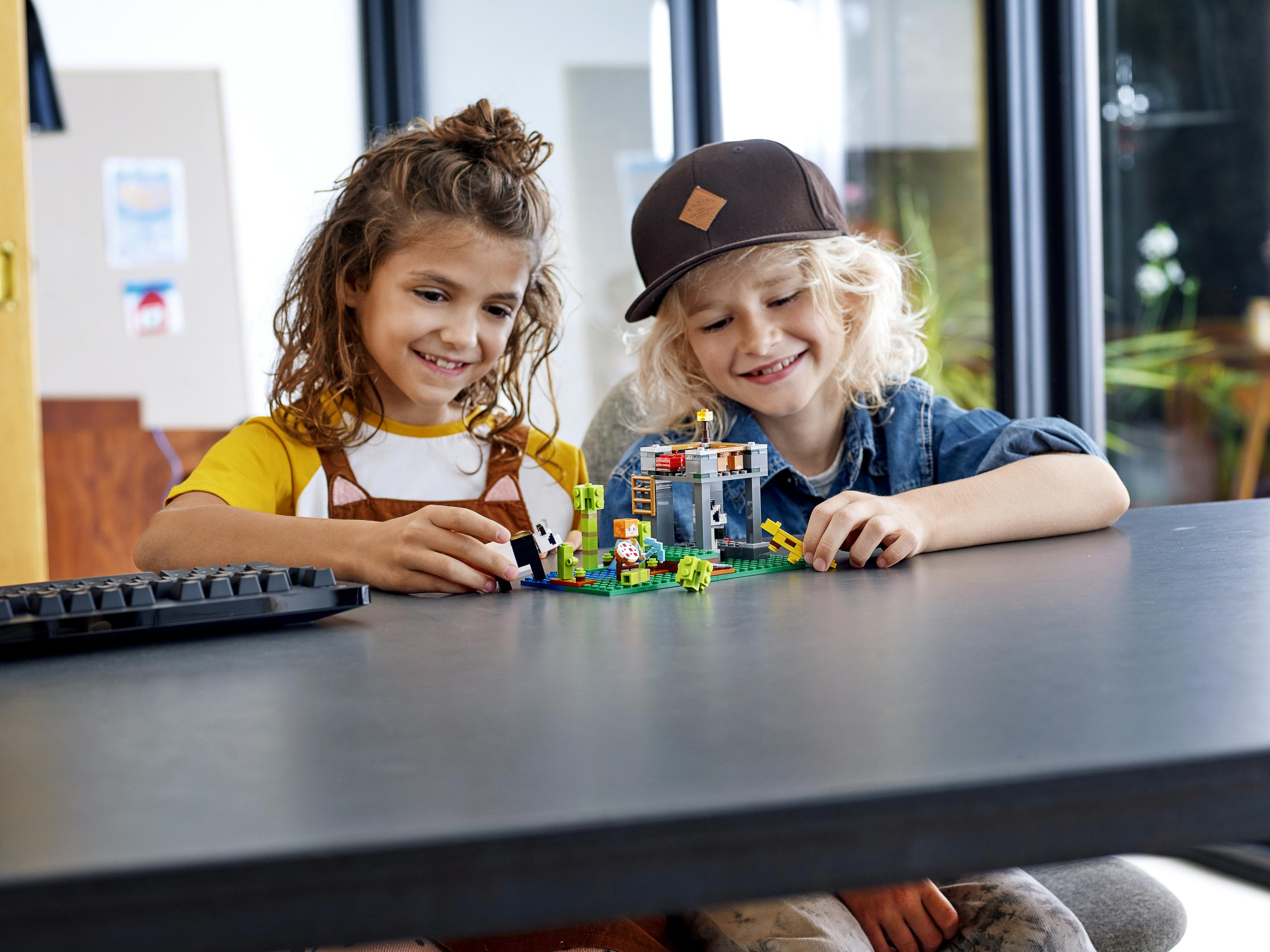 Dwoje dzieci bawiących się małym zestawem Lego na ciemnej powierzchni. Zestaw zawiera zielone klocki i małe figurki.