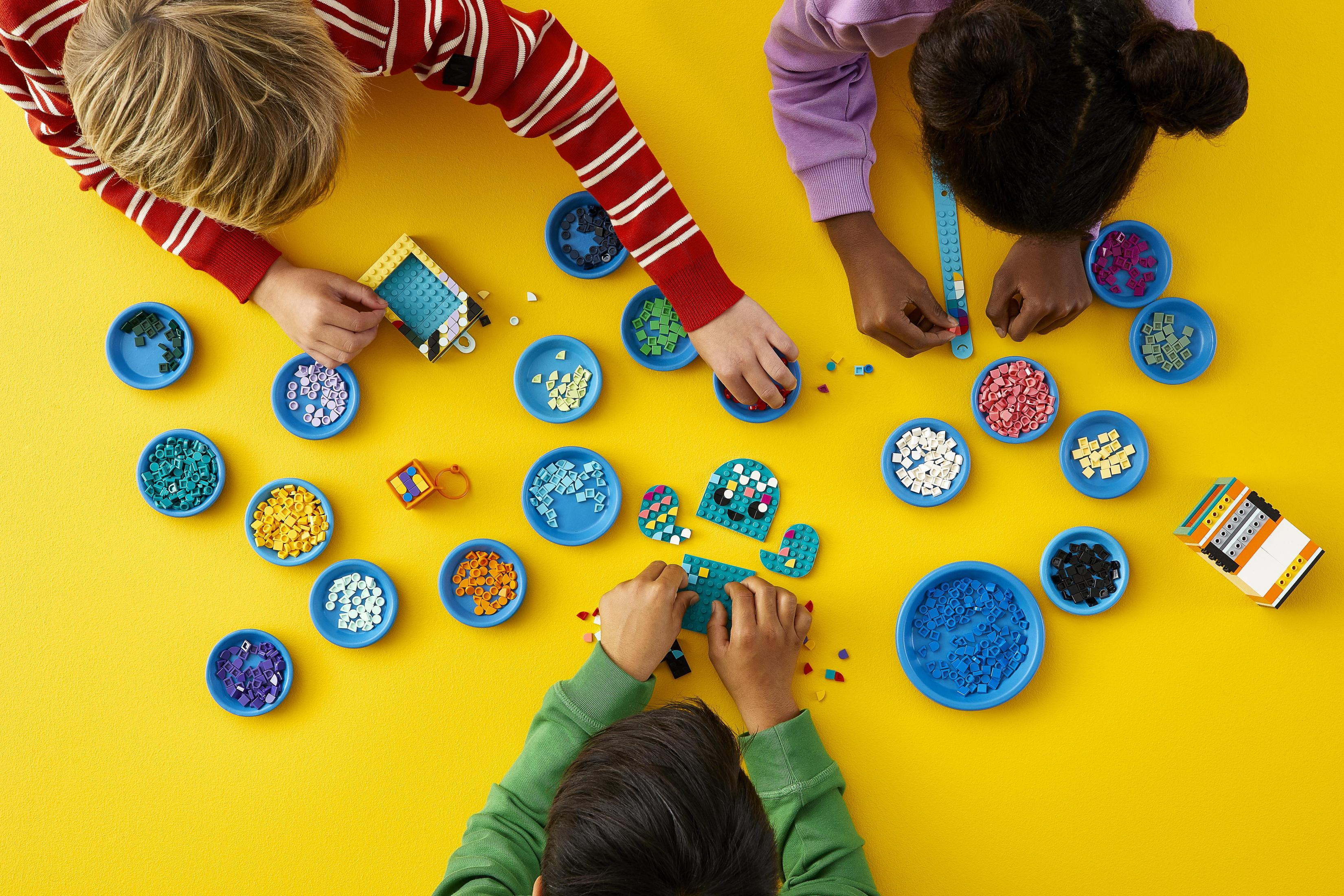 Dzieci bawią się kolorowymi klockami Lego, układając je w niebieskich miskach na żółtej powierzchni.