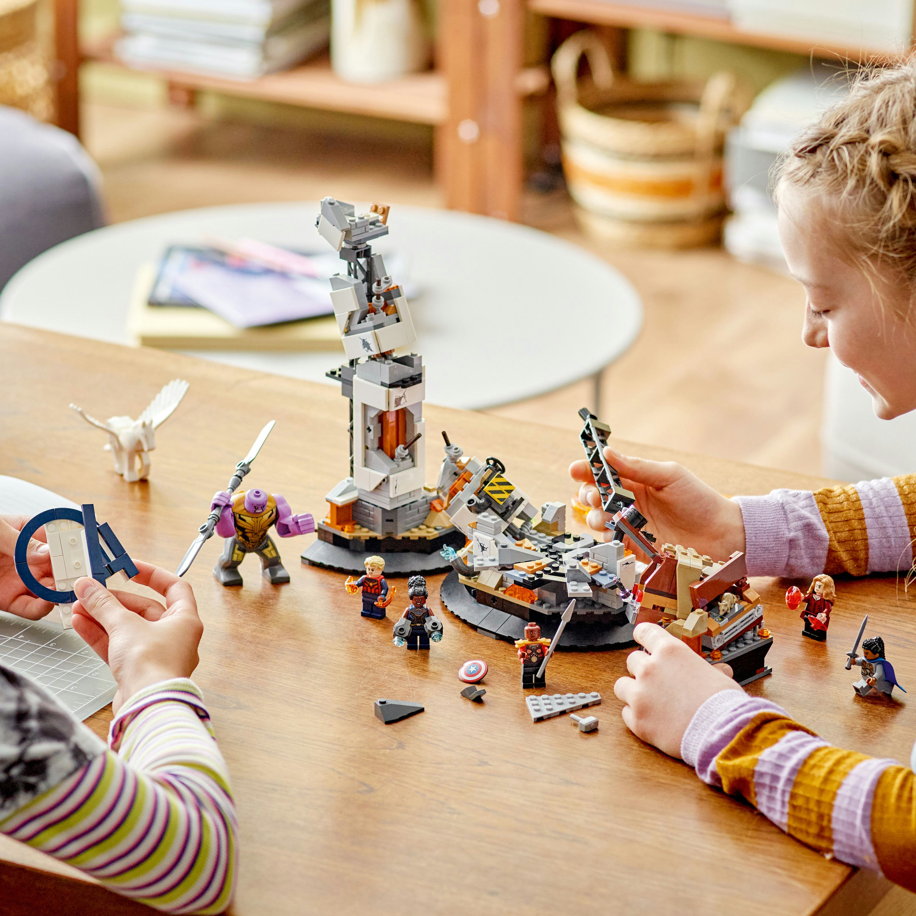 Zwei Kinder bauen ein Lego-Set mit Figuren und Strukturen auf einem Tisch.
