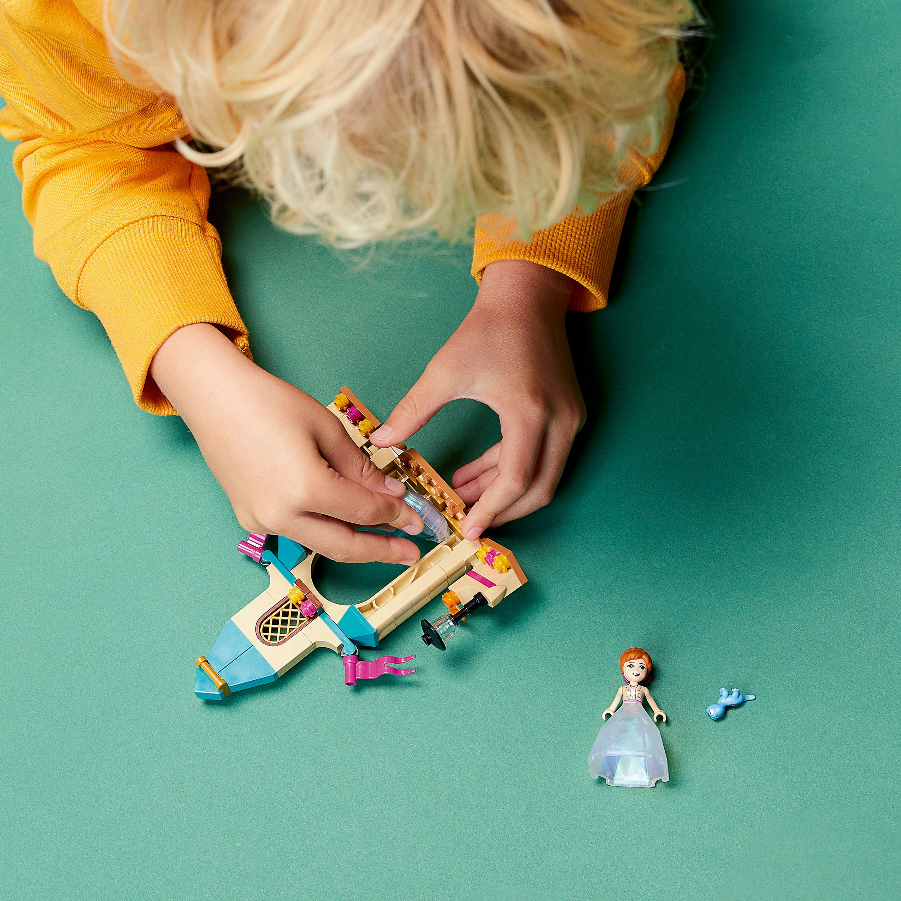 Mani di bambino che costruiscono un aereo giocattolo con mattoncini Lego, una bambola vicina.