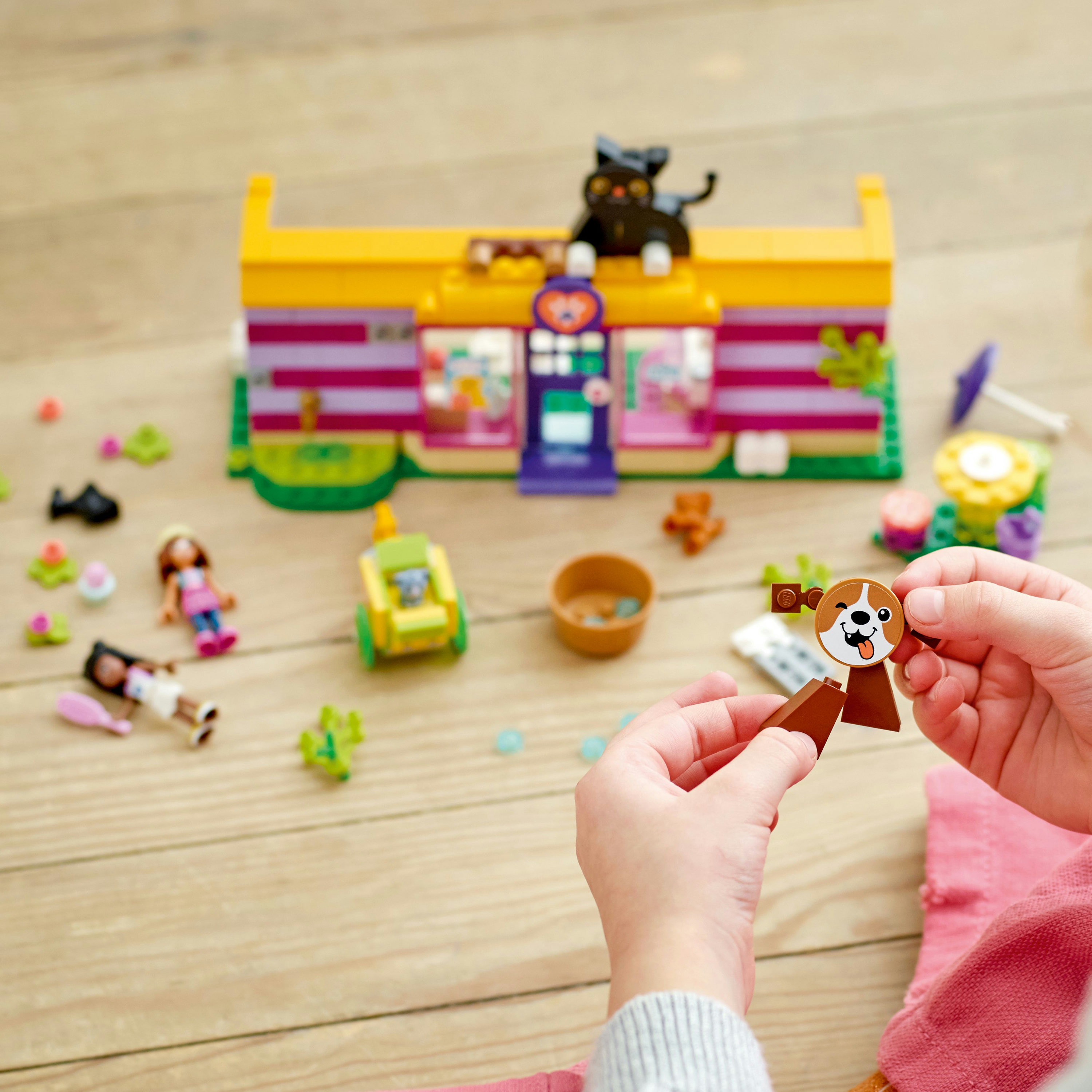 Hände halten einen LEGO-Hund, im Hintergrund ein LEGO-Geschäft und Minifiguren.