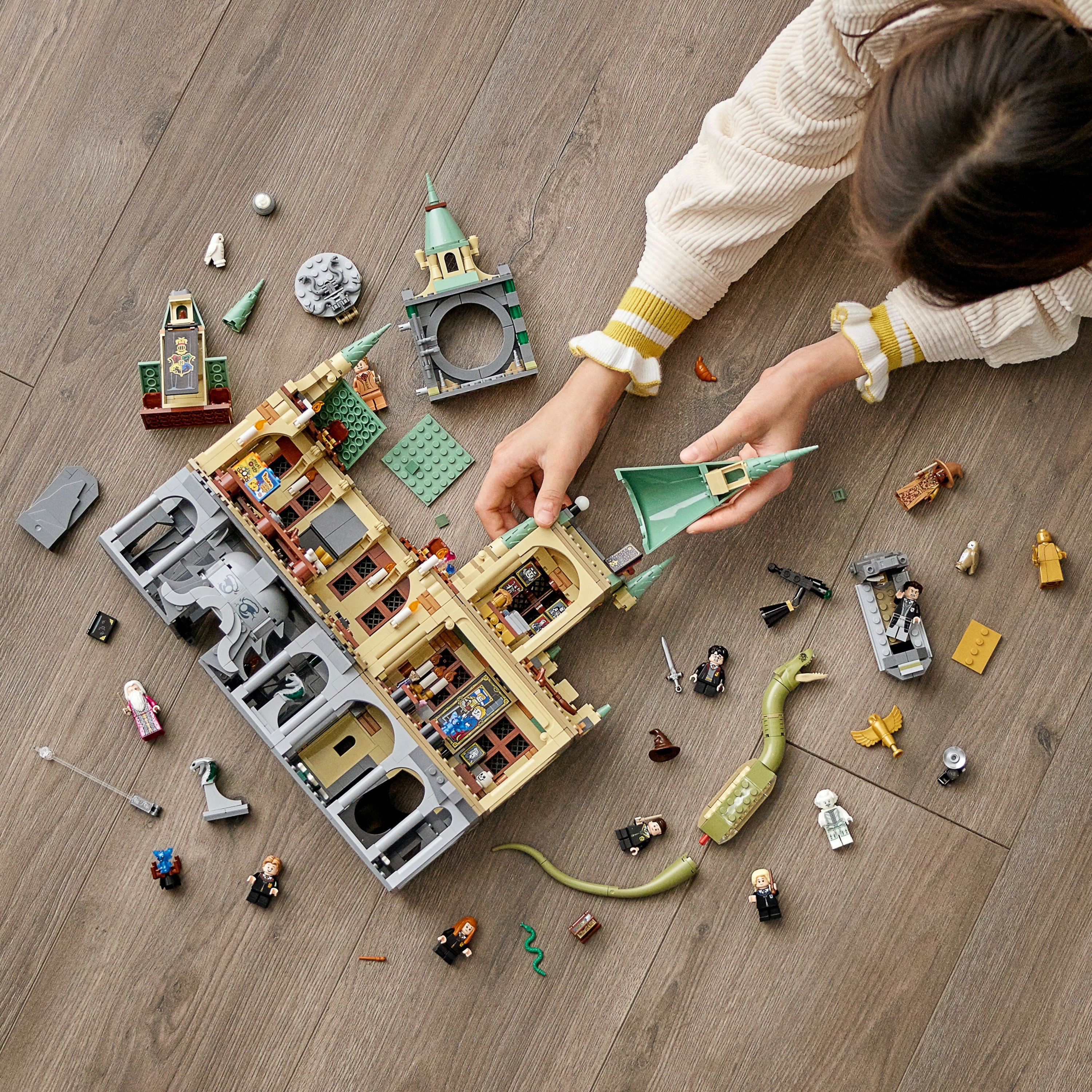 Una persona assembla un grande set LEGO di Harry Potter. La scena è un pavimento in legno con vari pezzi LEGO sparsi.