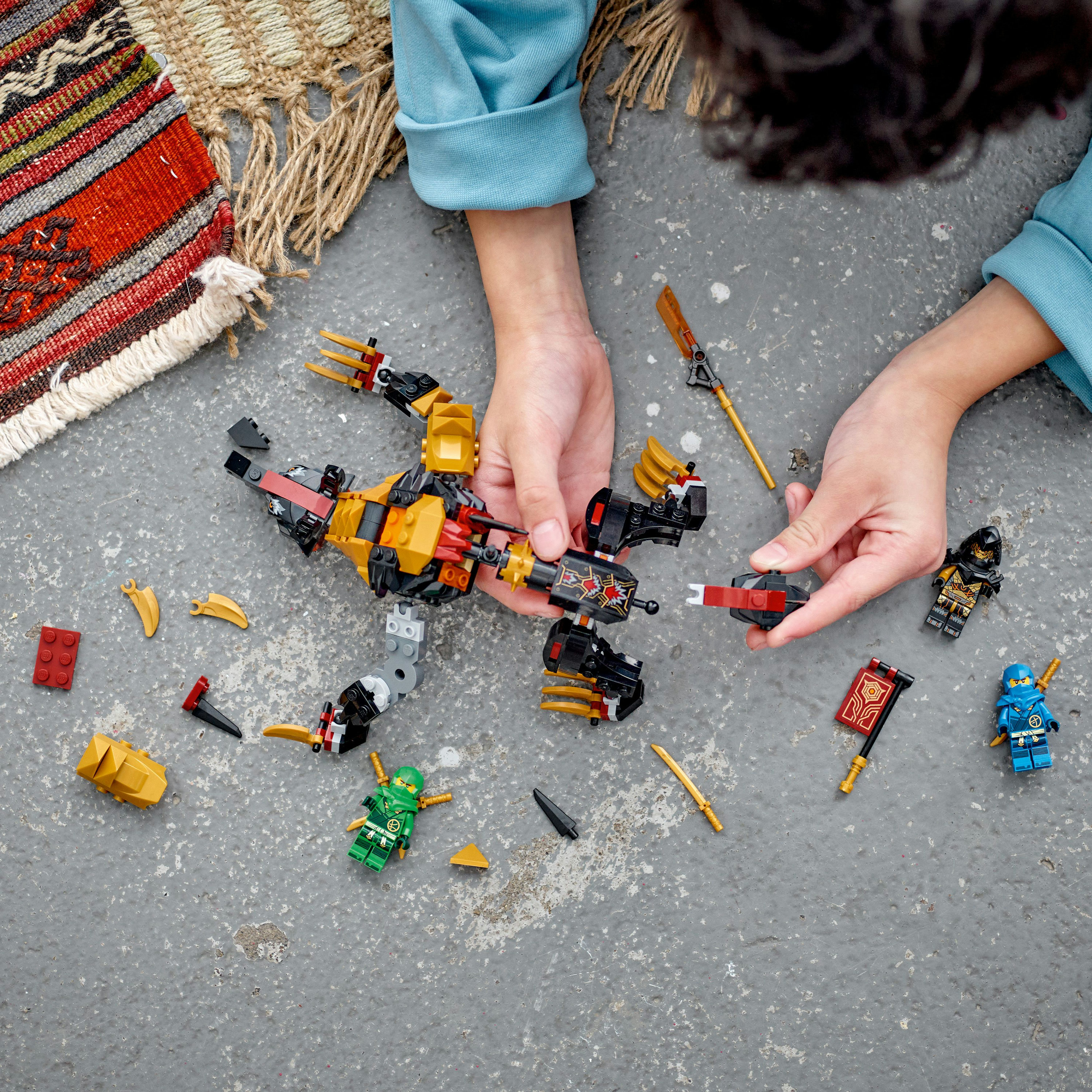 Manos ensamblando un set de Lego con minifiguras y piezas de Lego sobre una superficie gris, con piezas dispersas.