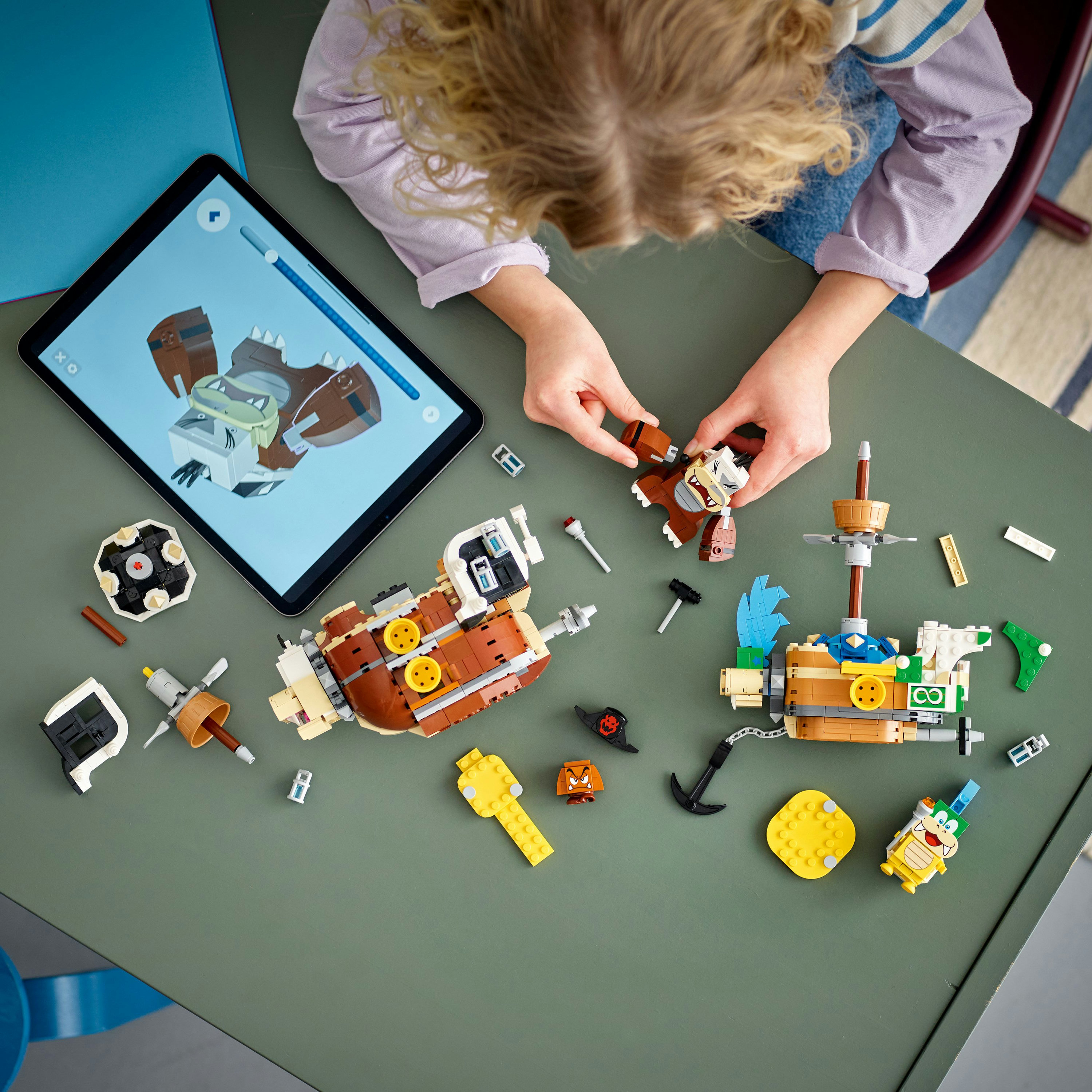 Dziecko składające łódź Lego, z tabletem z instrukcjami w pobliżu, na zielonej powierzchni.