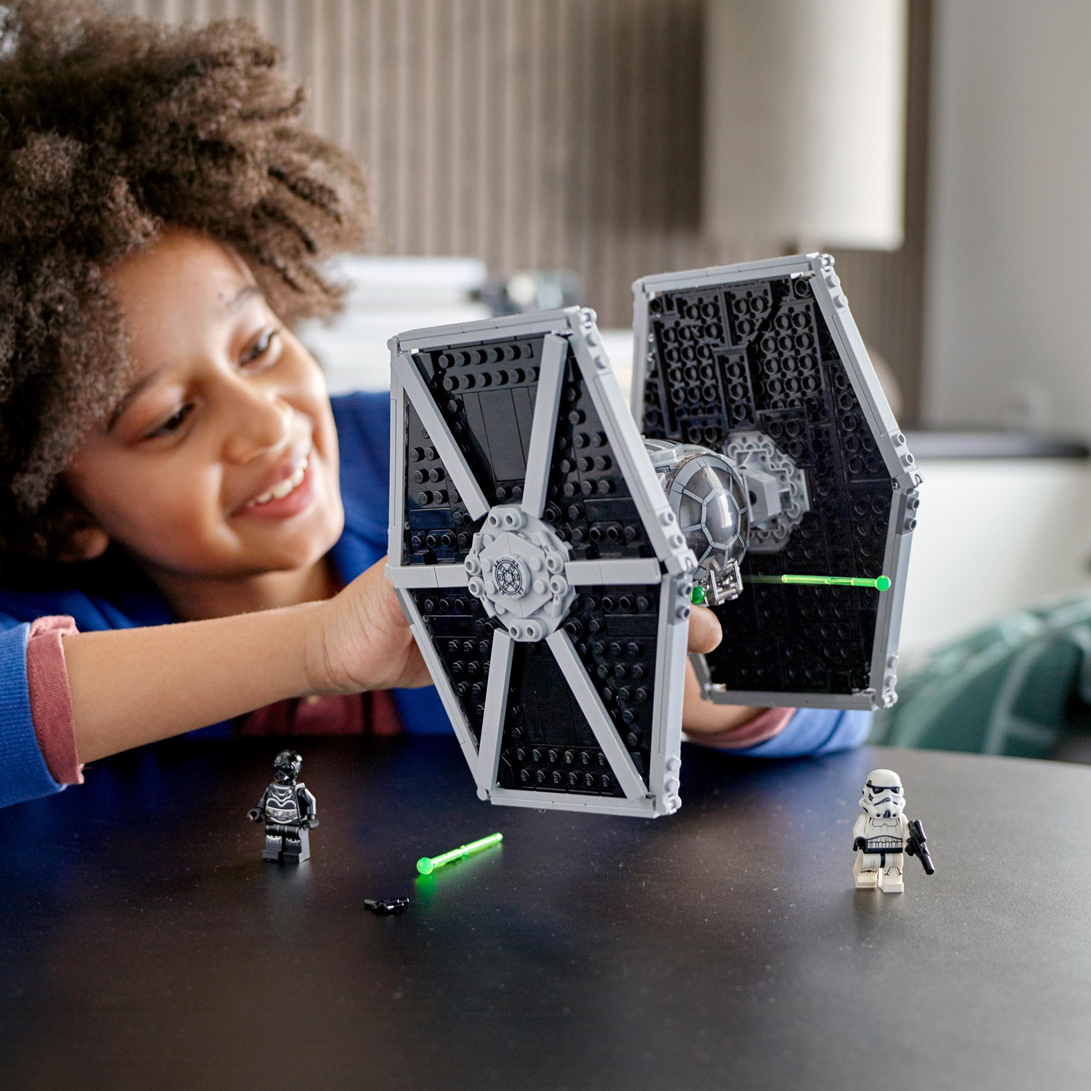 Genç bir çocuk, Lego Star Wars TIE Fighter tutarken gülümsüyor. İki minifigür ve yeşil bir ışın kılıcı mevcut.