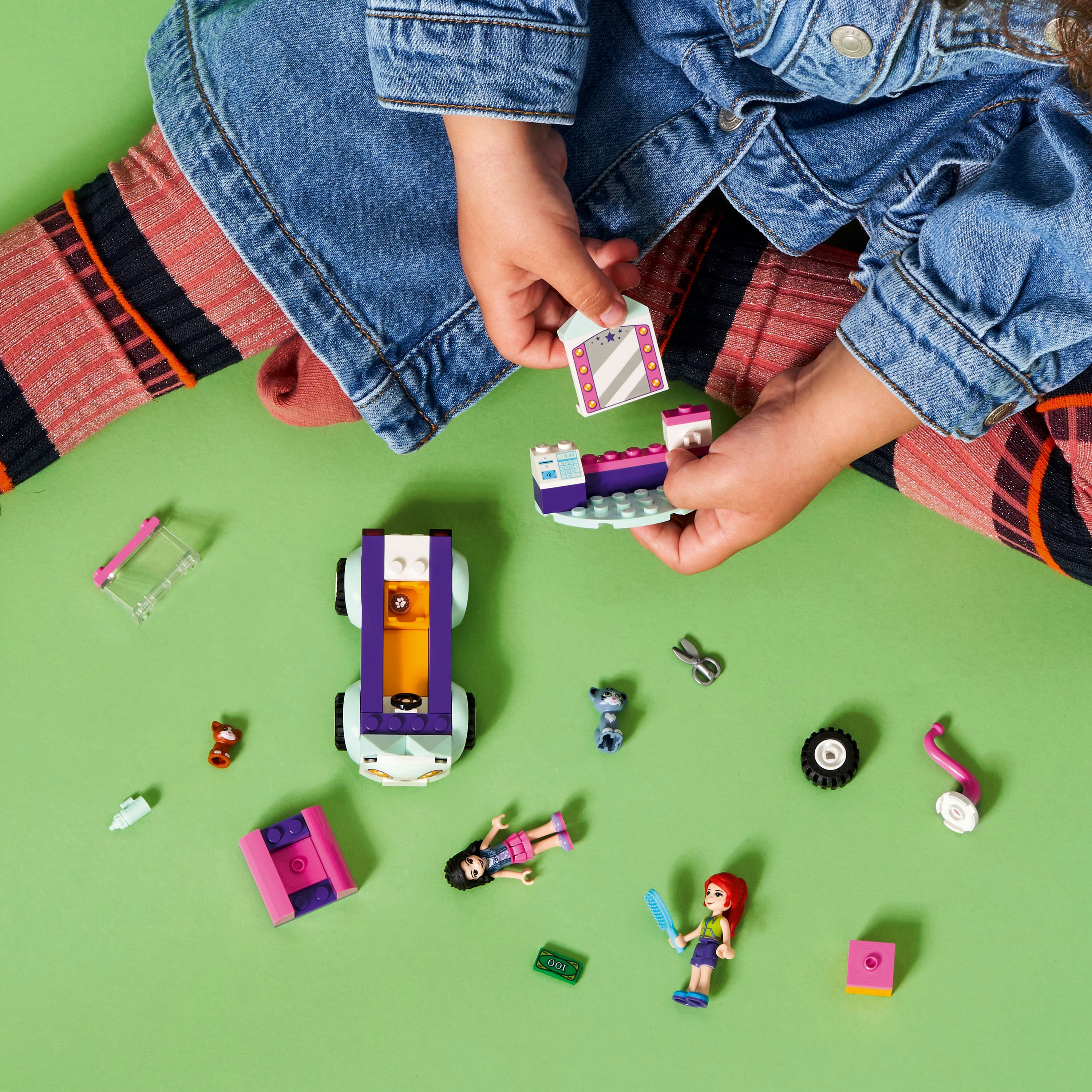 Kind, das ein Lego-Set auf einer grünen Oberfläche zusammenbaut. Es enthält Figuren, ein Auto und Bauteile.