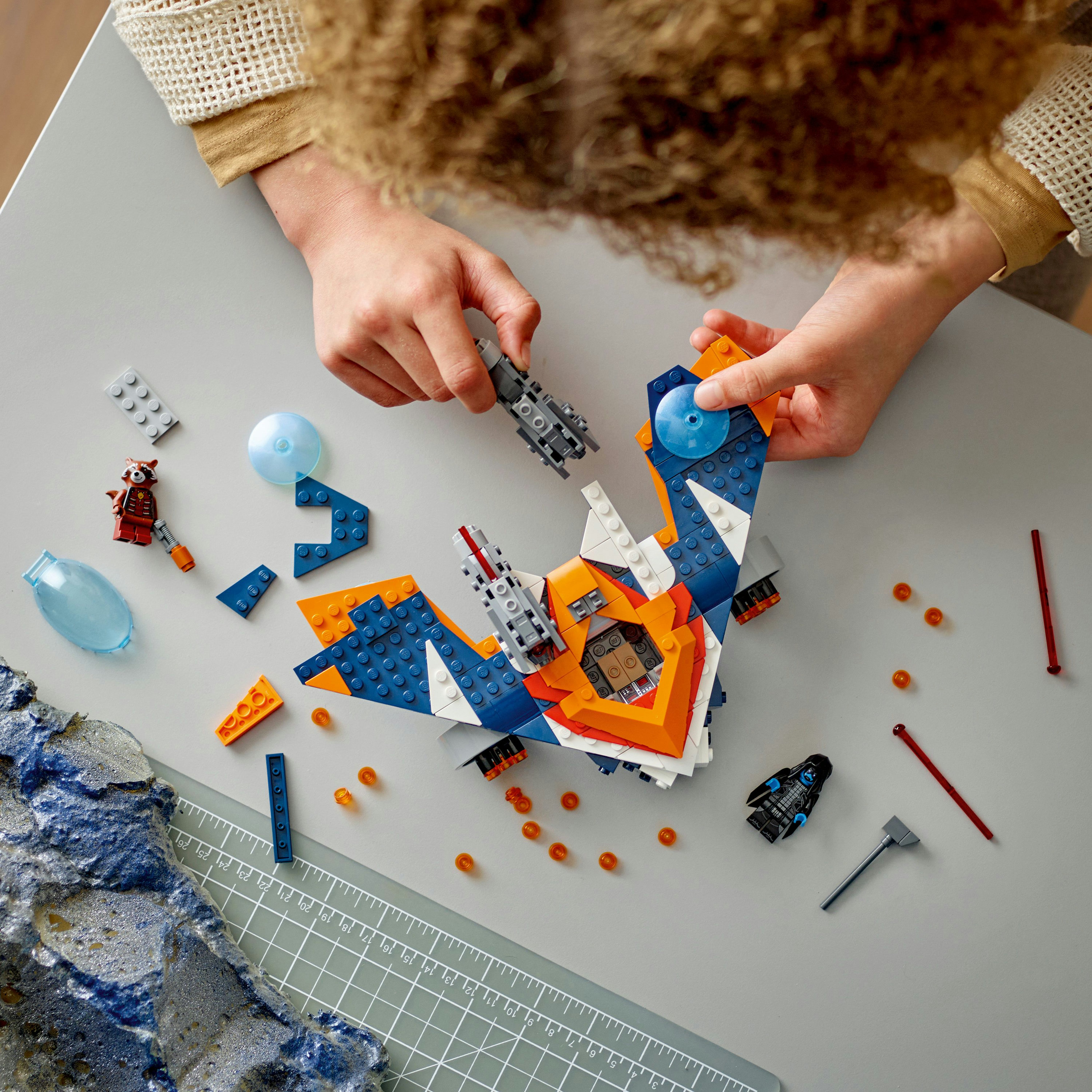 Eller, gri bir yüzeyde dağınık parçalarla bir Lego uzay gemisi topluyor.