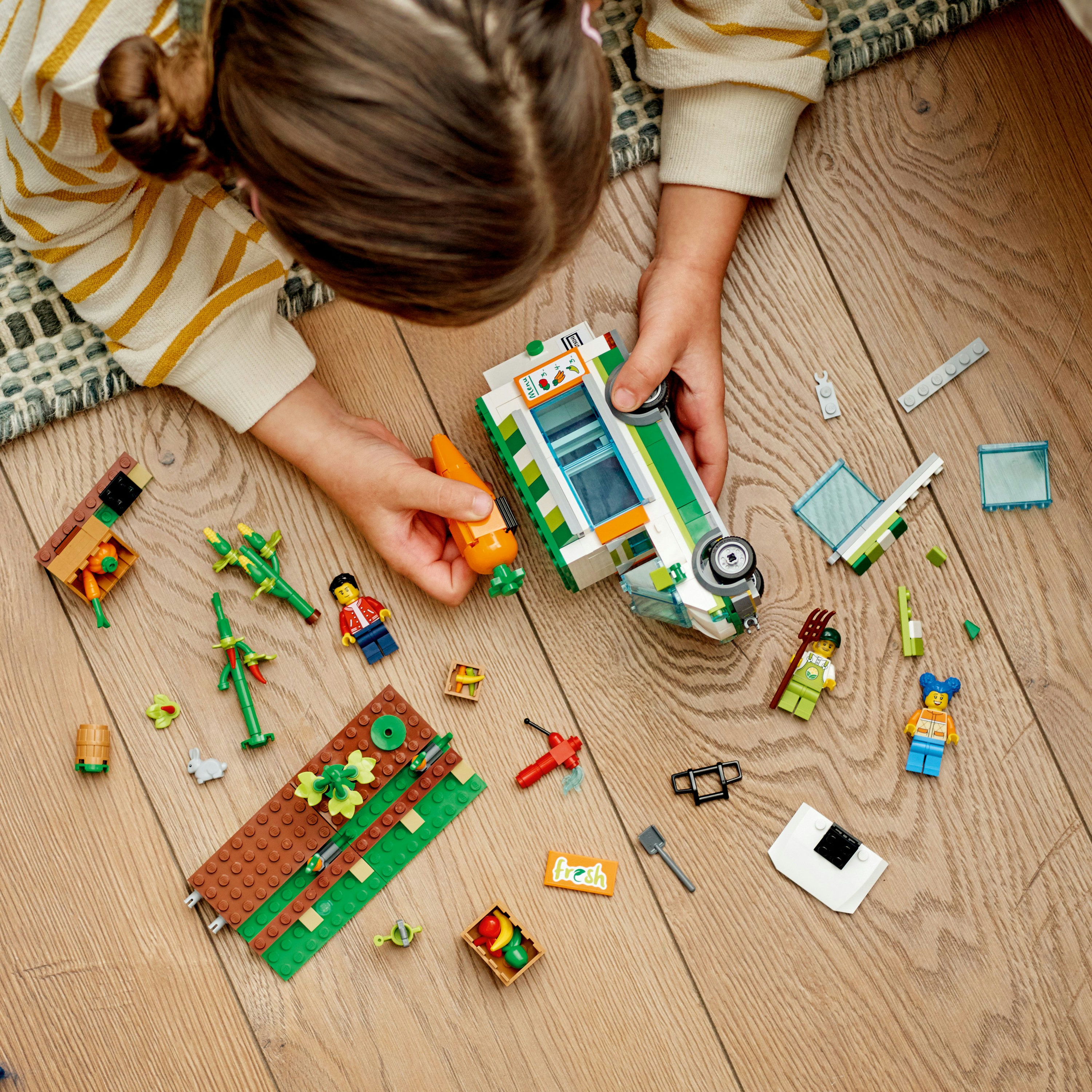 Dziecko składające zestaw Lego na drewnianej podłodze. Zestaw wygląda na food trucka.