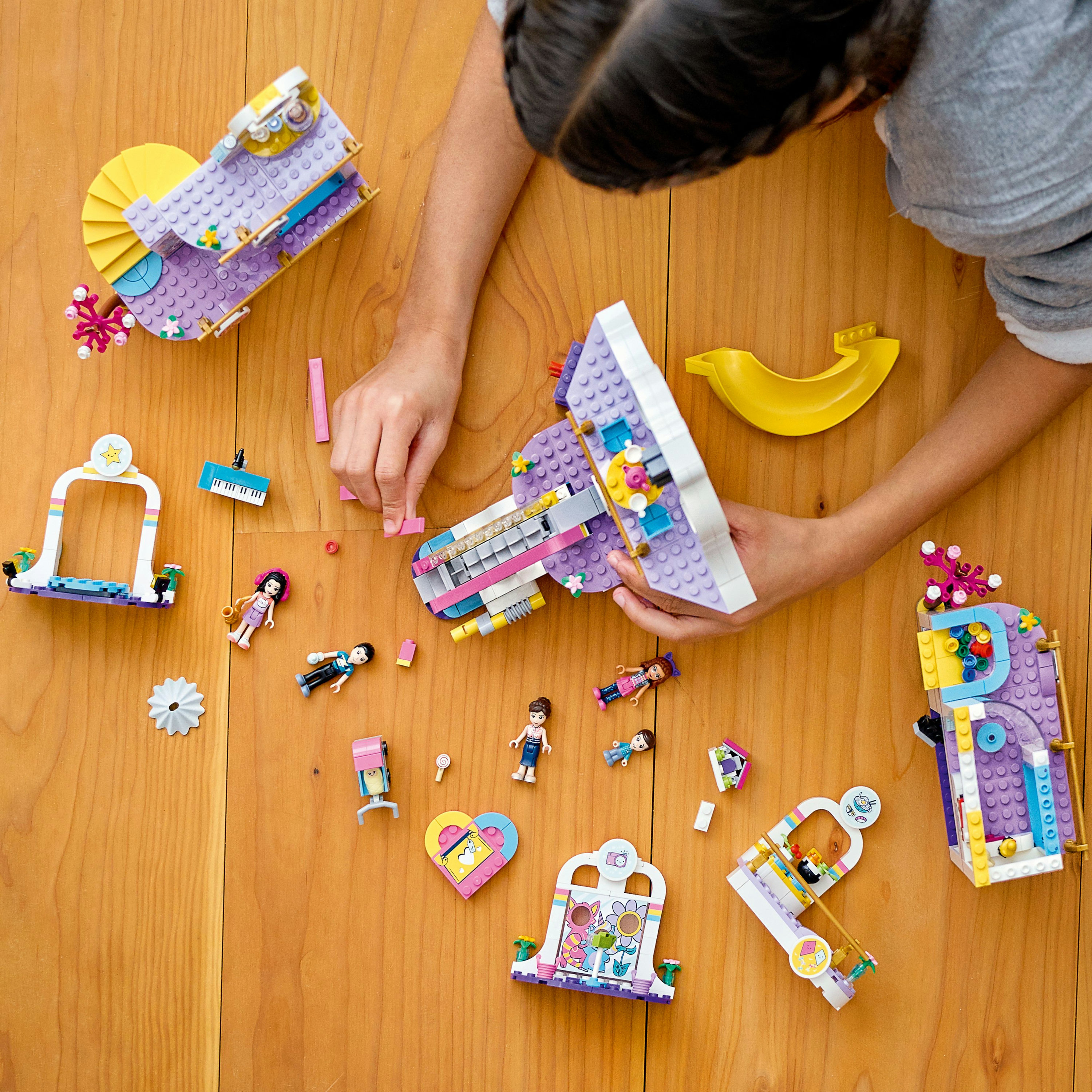 Kinderhände bauen LEGO Friends Set auf Holzoberfläche.