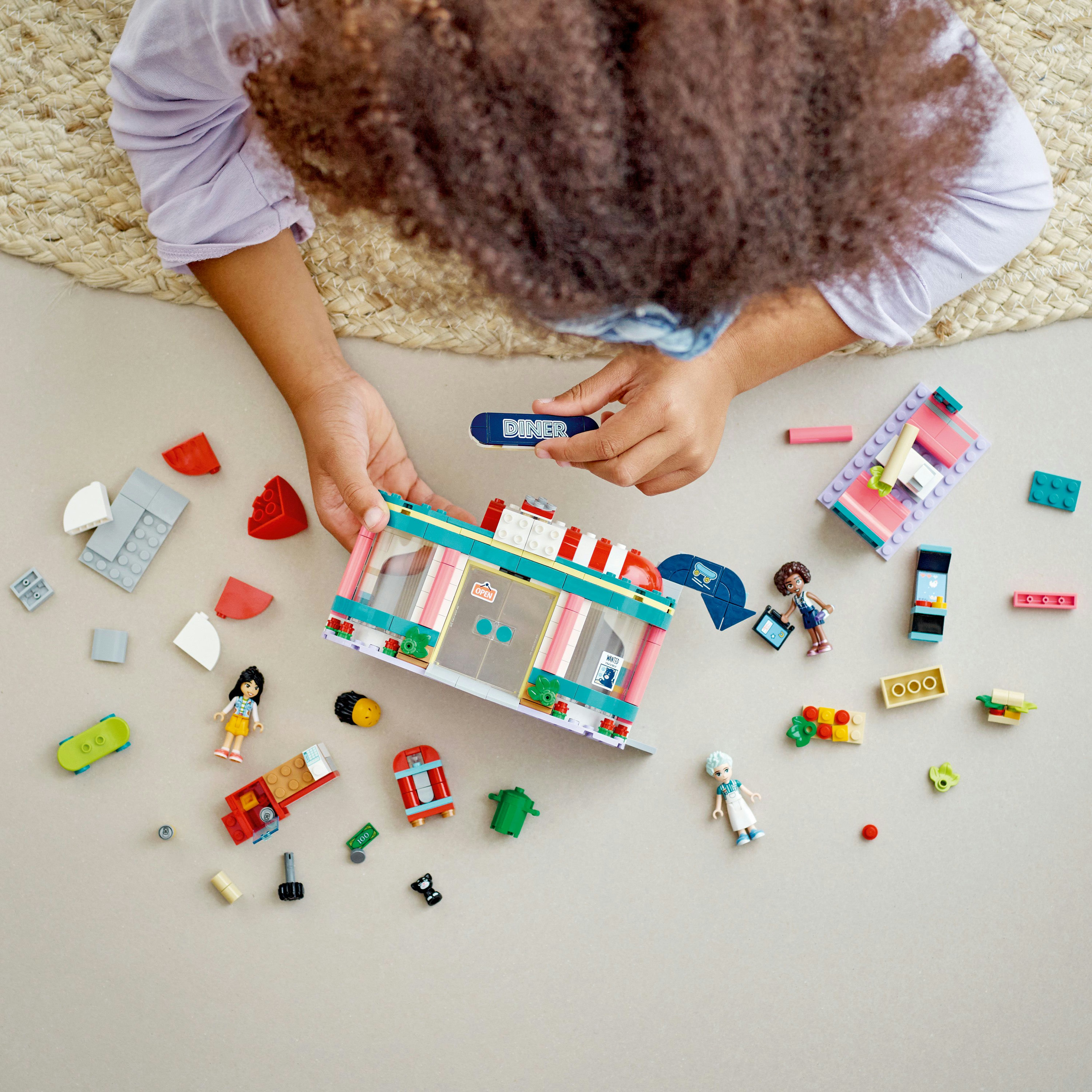 Kind baut ein Lego-Restaurant mit Figuren und einem Skateboard. Viele Legosteine ​​sind verstreut.