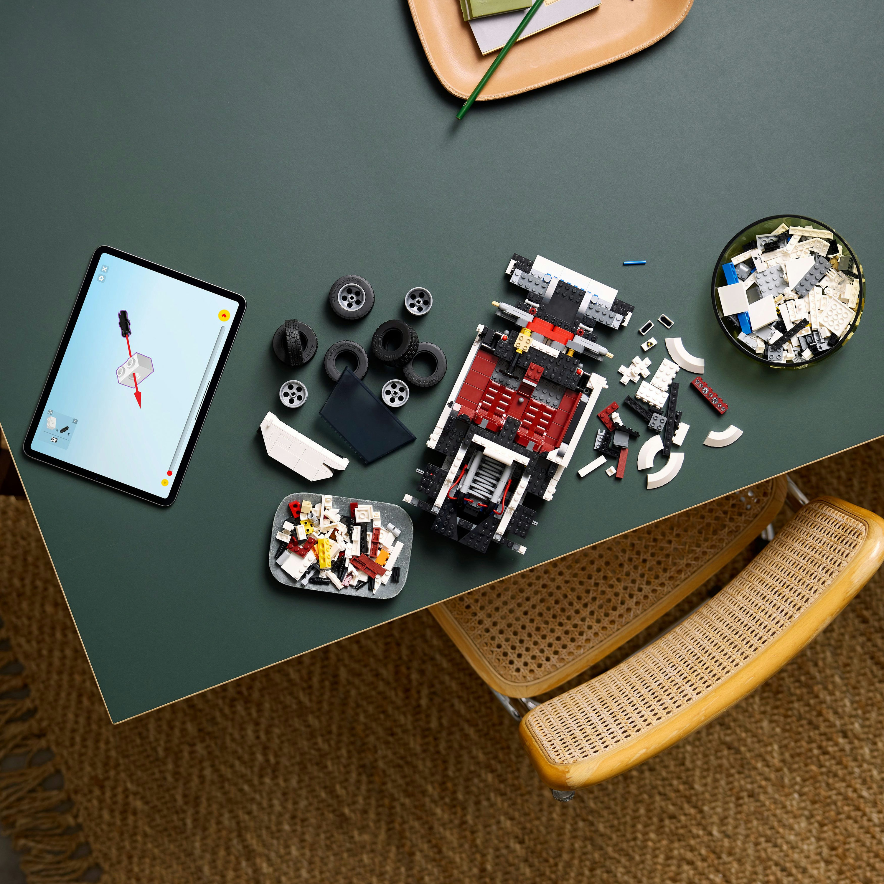 Widok dziecka na części samochodu Lego i instrukcje na zielonym stole, gotowe do montażu.