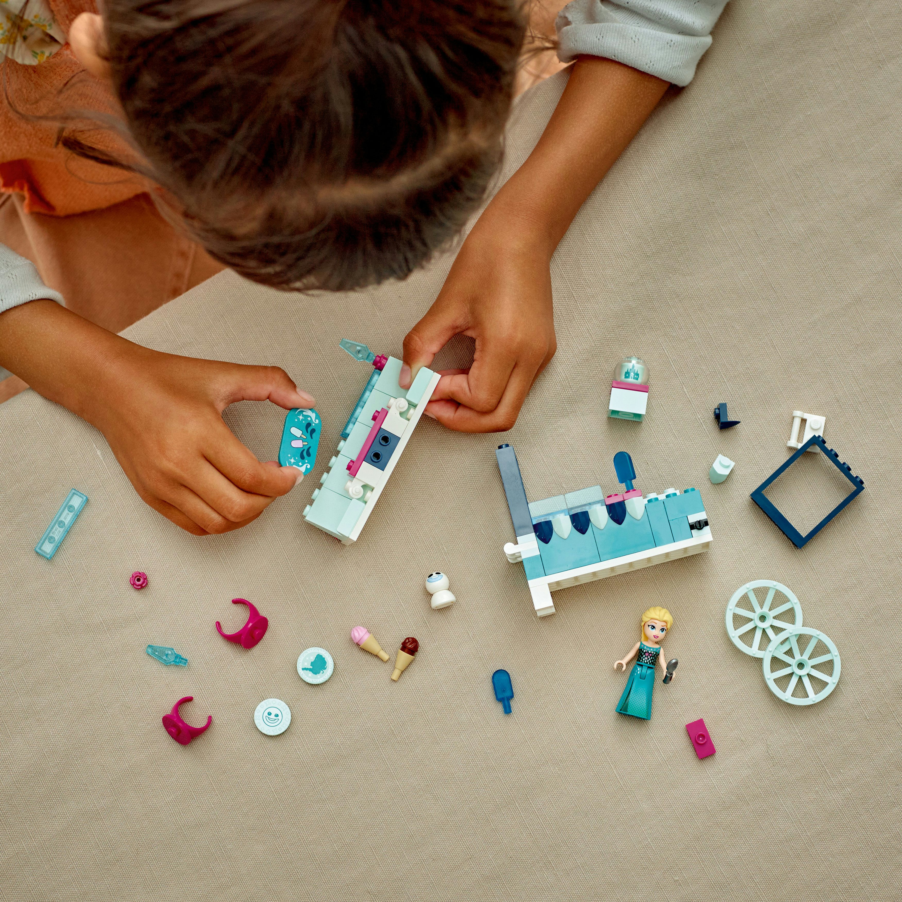 Kind hantiert Lego-Set mit Miniaturboot, Figuren und Zubehör auf beiger Oberfläche.