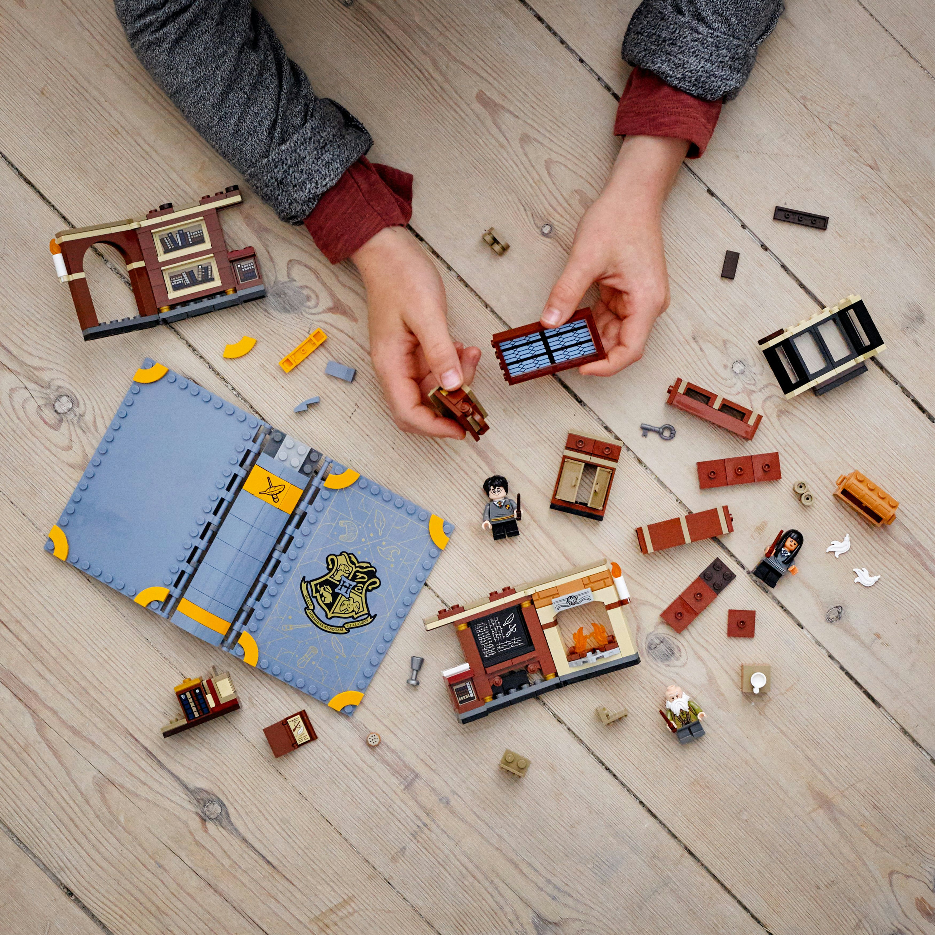 Hände, die Lego-Teile zusammensetzen. Das Set enthält ein Buch, Figuren und Bauelemente. Die Oberfläche ist Holz.