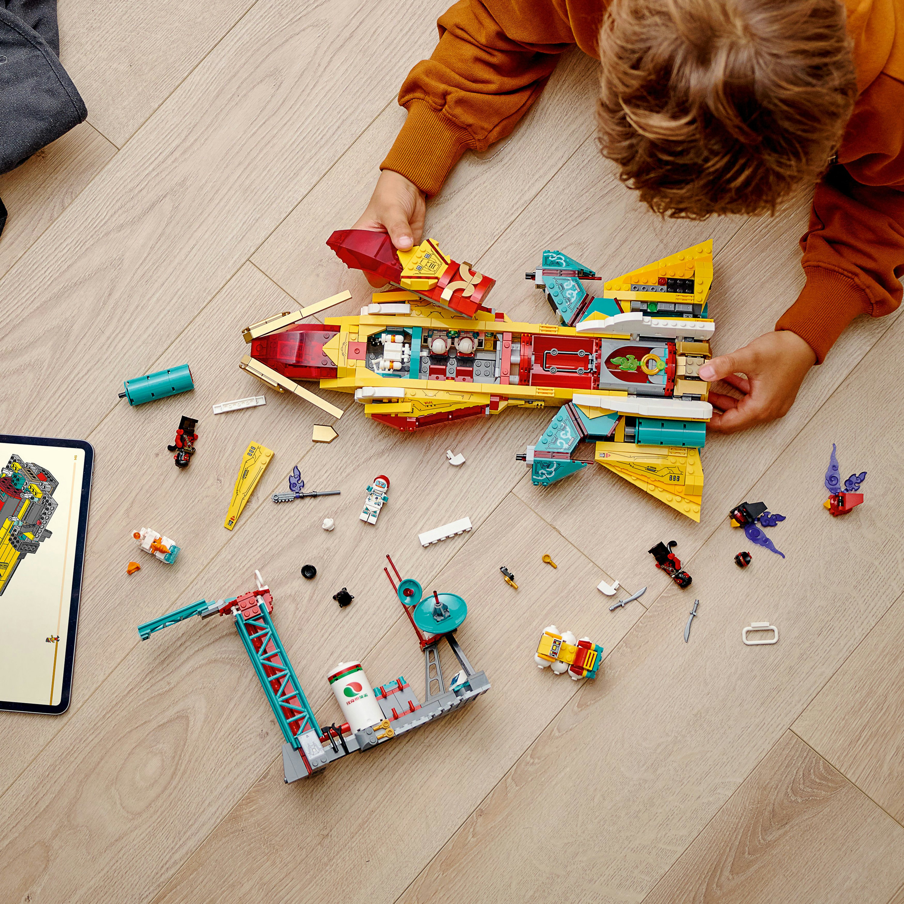 Çocuk Lego uzay gemisi yapıyor. Set sarı, kırmızı ve deniz mavisi renginde ve figürler içeriyor.