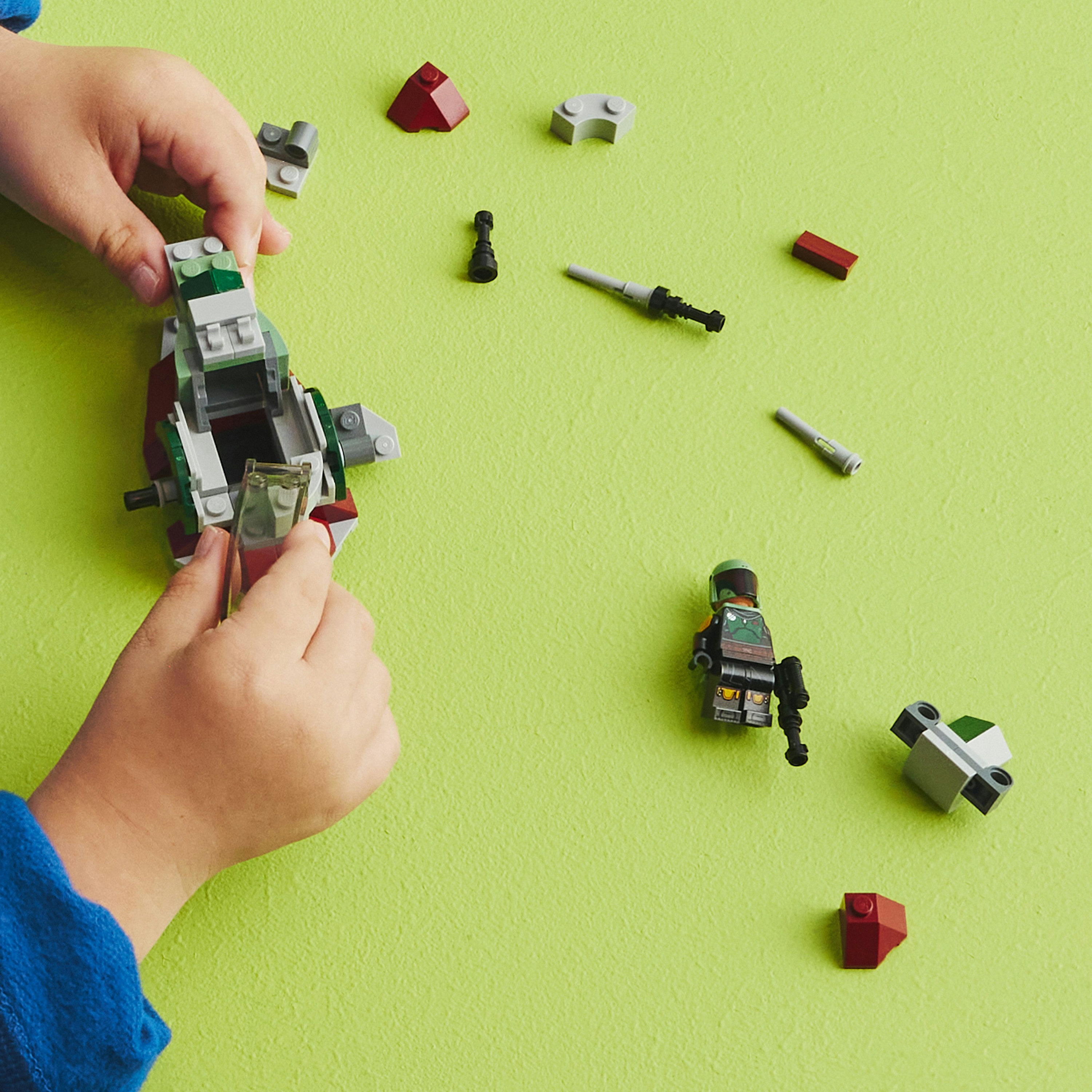 Manos construyen un set de Lego Star Wars sobre una superficie verde con piezas dispersas.