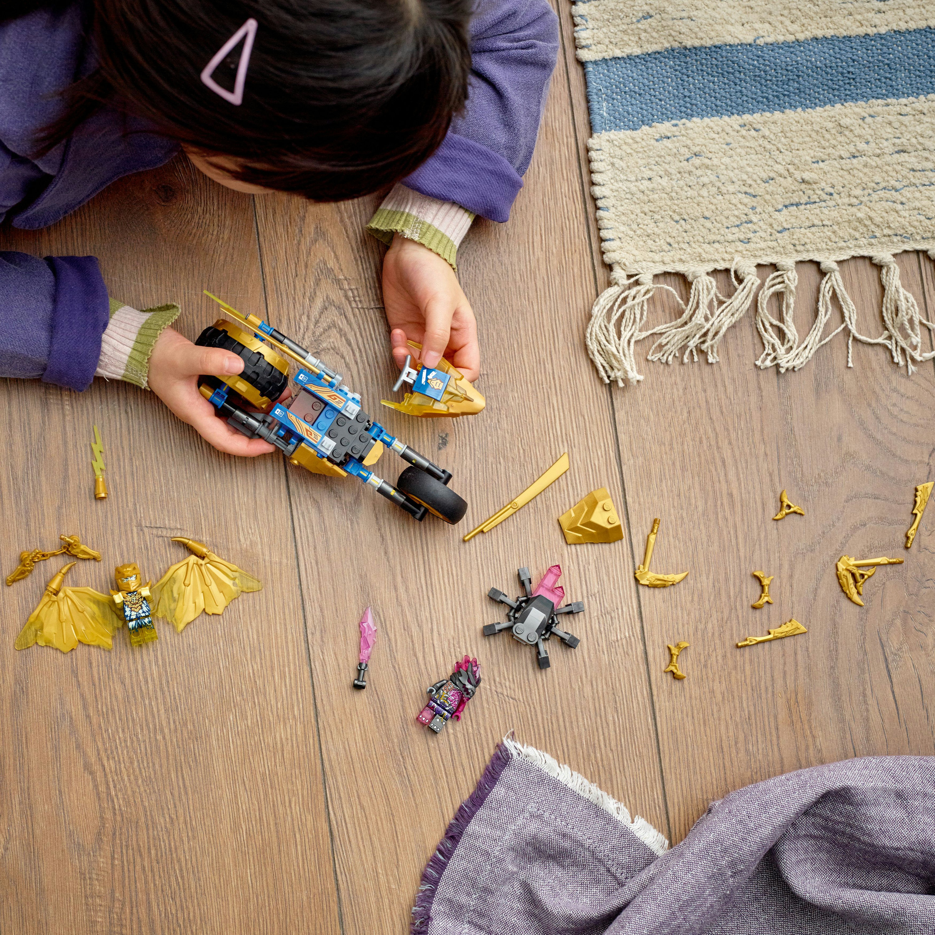 Ein Kind spielt mit einem Lego Ninjago Set, das ein blaues und goldenes Motorrad und Figuren zeigt.