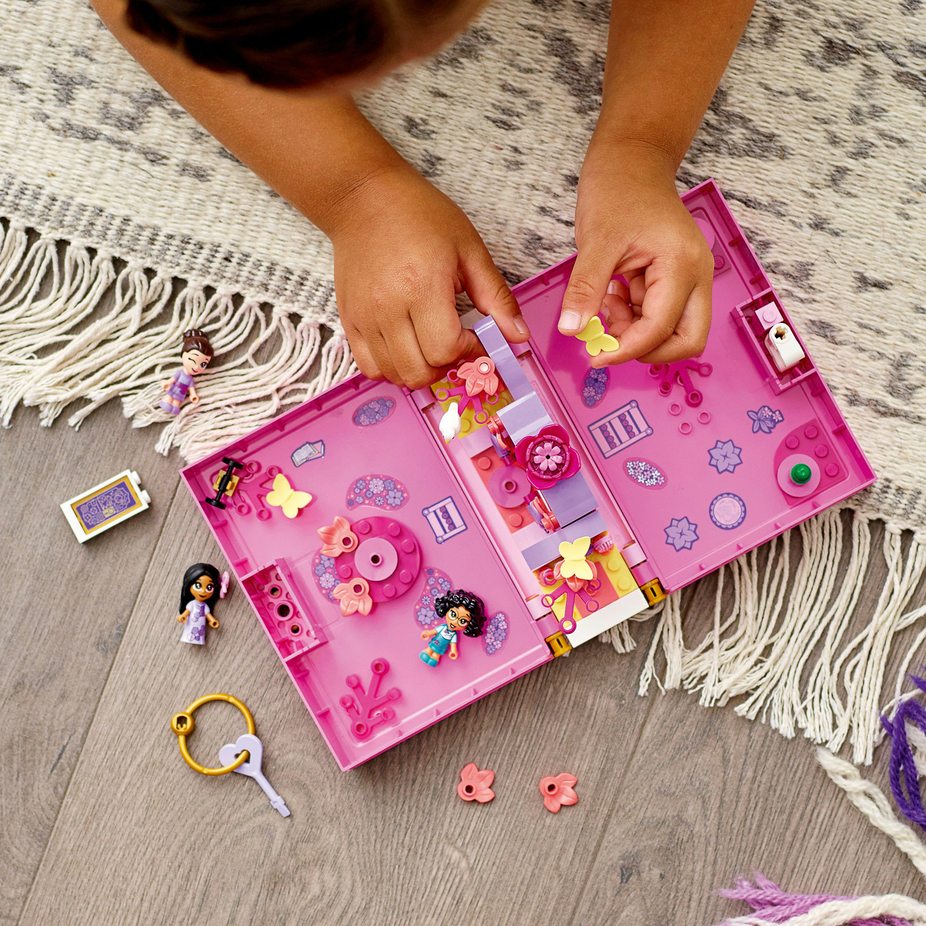 Çocuğun elleri, mini figürler, çiçekler ve pembe bir çanta ile LEGO Friends setini ahşap bir zemine yerleştiriyor.