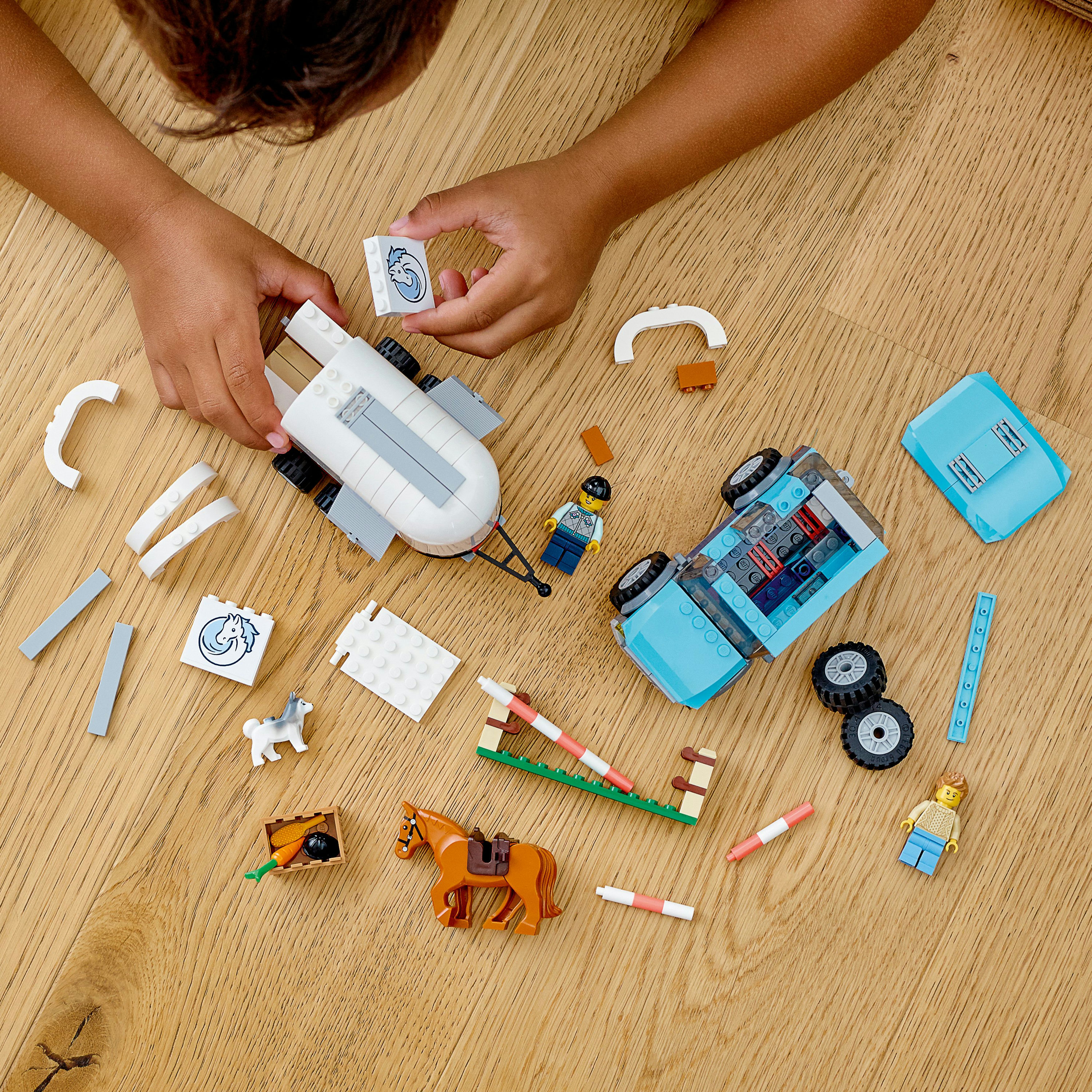 Un bambino sta costruendo un set Lego con un rimorchio e un'auto, insieme a vari accessori su un pavimento di legno.