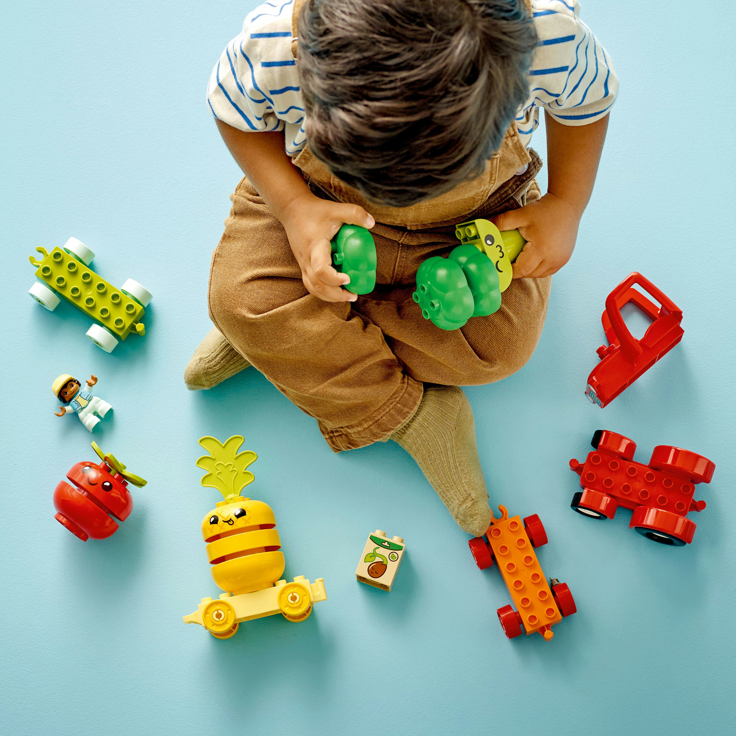 Un bambino che gioca con veicoli giocattolo Lego Duplo e mattoncini a tema cibo su una superficie blu.