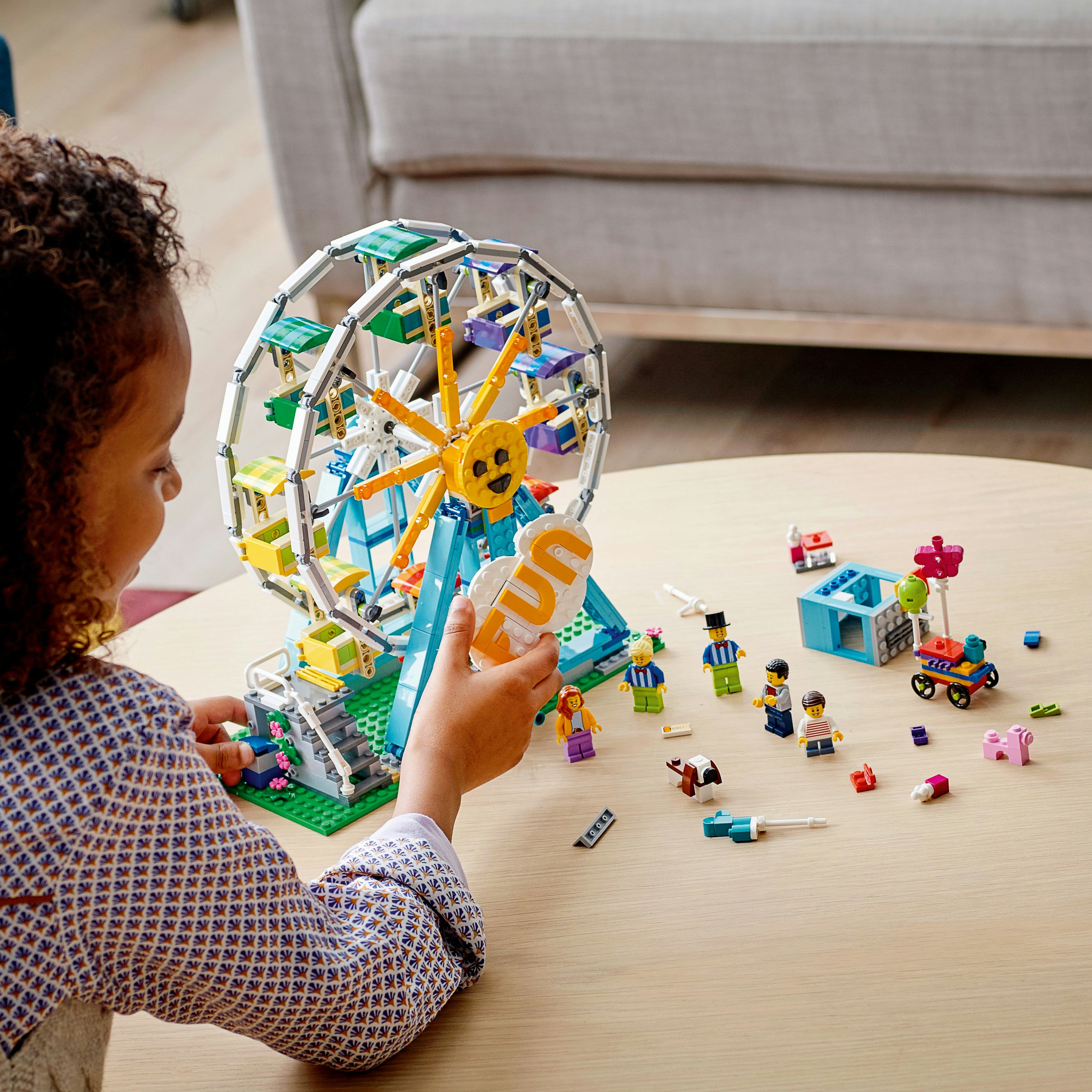 Una bambina gioca con un set Lego di una ruota panoramica, con personaggi, accessori ed elementi colorati.