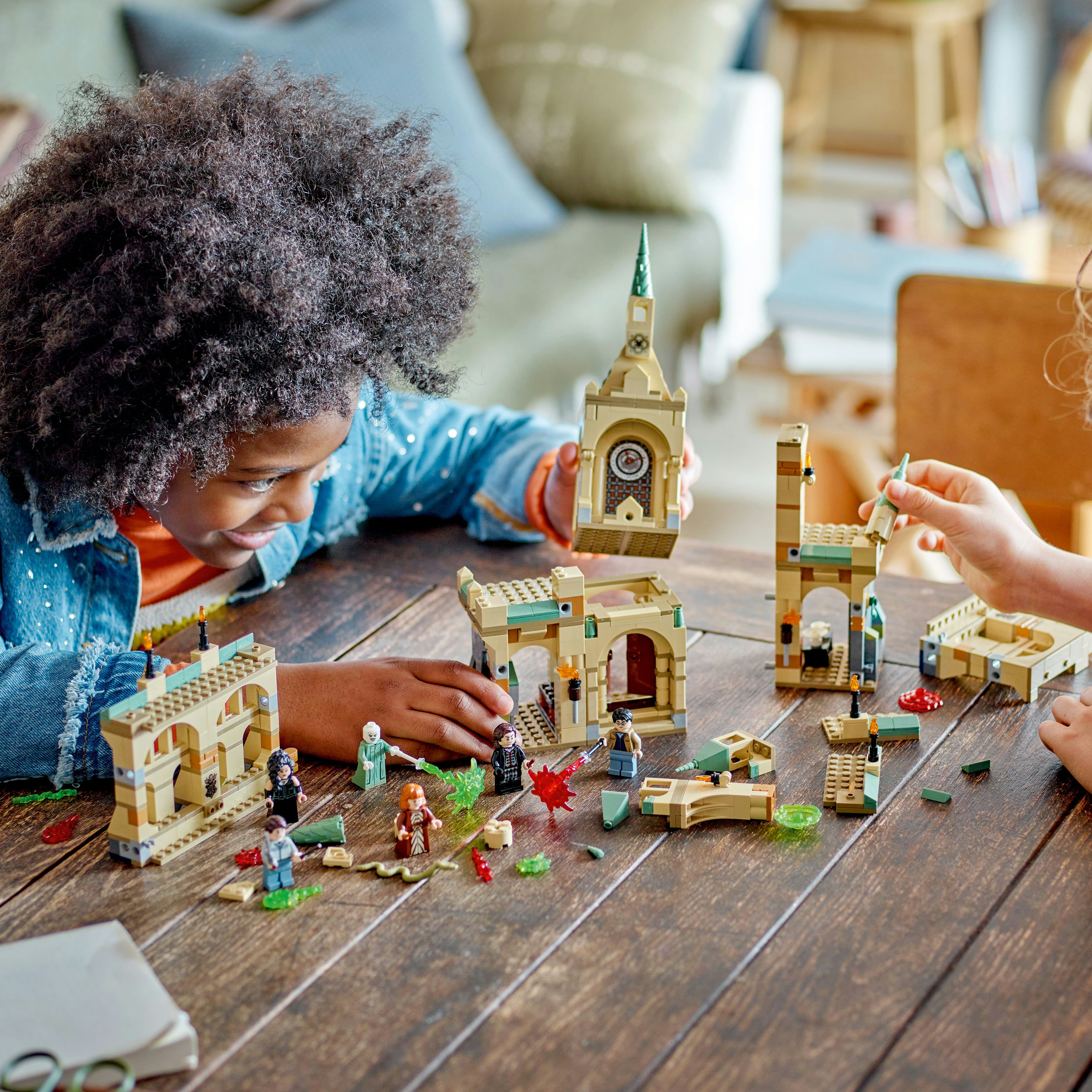 Kinder spielen mit einem LEGO Harry Potter Set auf einem Holztisch. Die Szene enthält LEGO-Figuren und Bauteile.