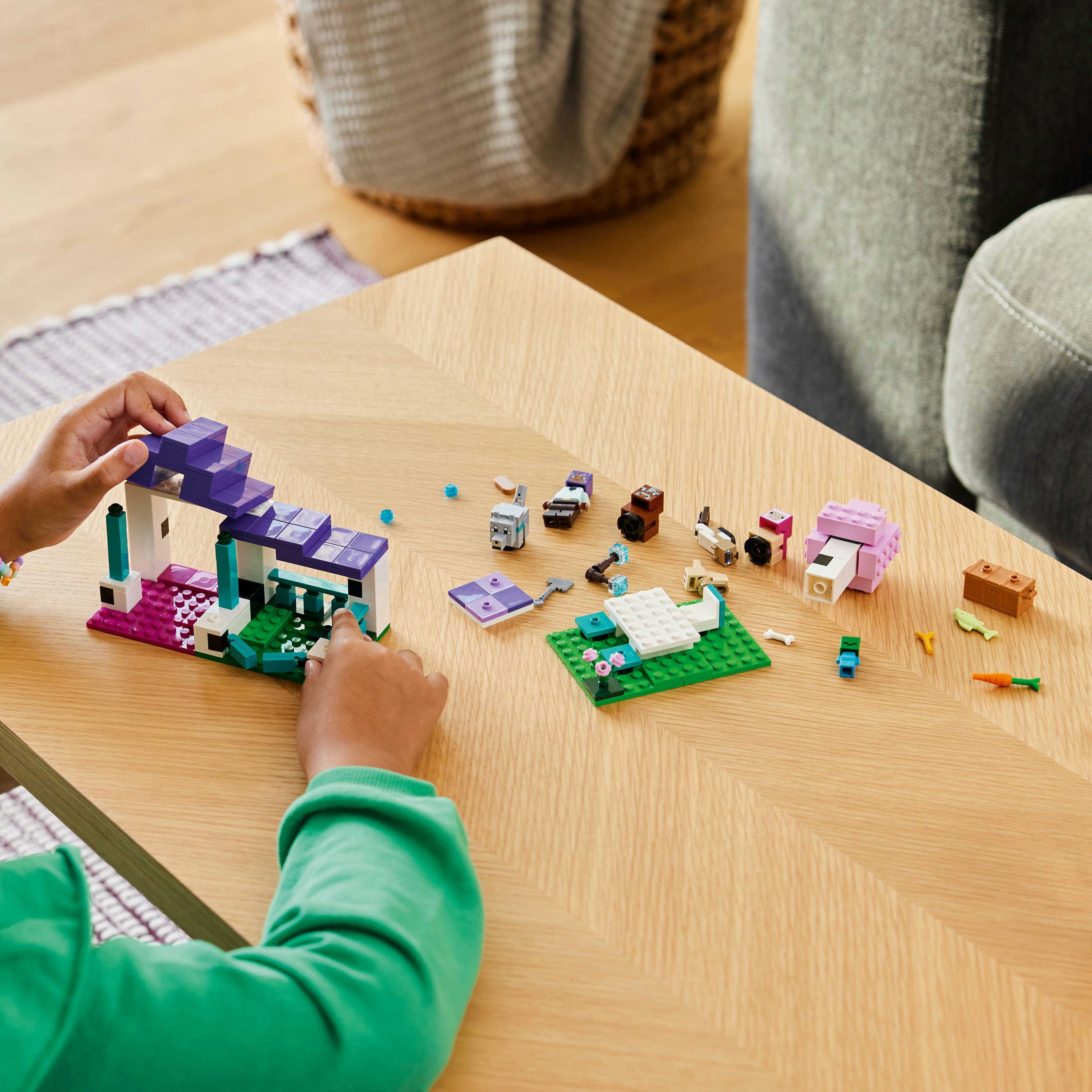 Mani di un bambino costruendo una casa Lego Minecraft su un tavolo di legno.