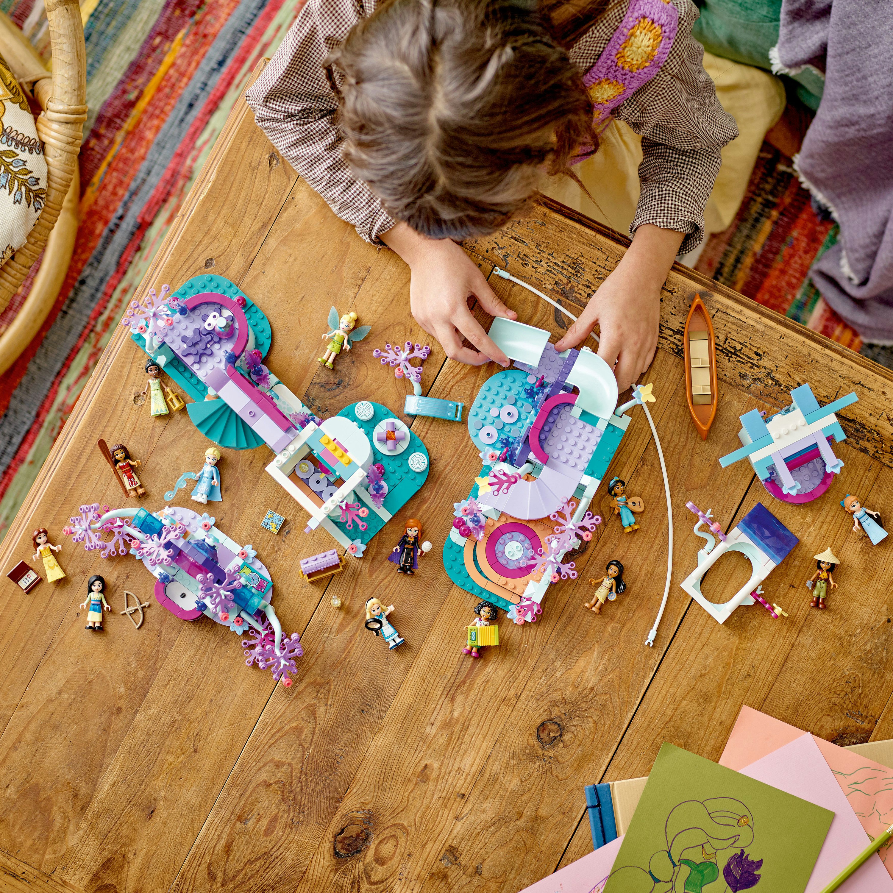 Kind spielt mit Lego Friends. Spielzeug und Figuren auf einem Holztisch, baut eine kreative Szene.