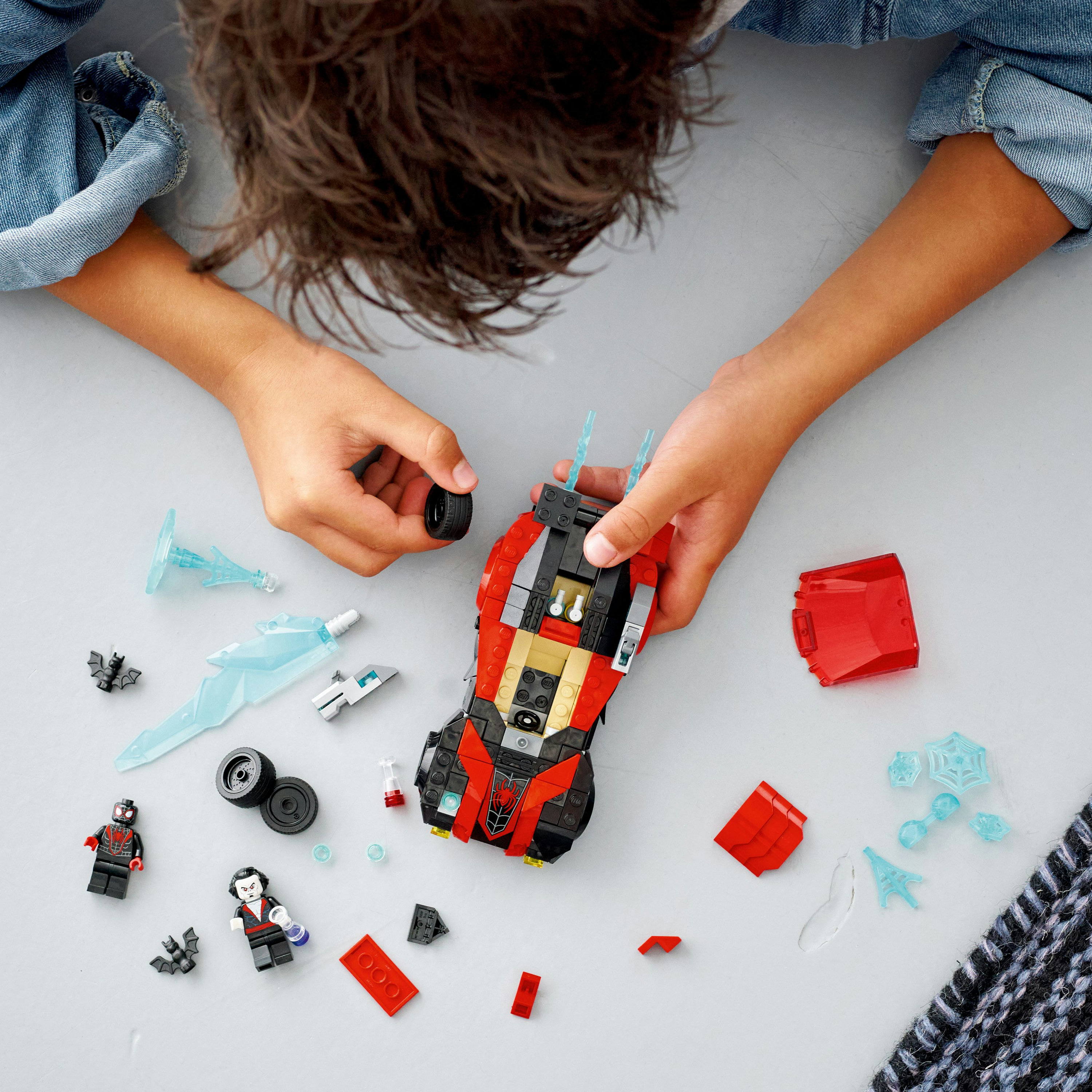 Kind mit Lego-Teilen baut ein rot-schwarzes Rennauto.